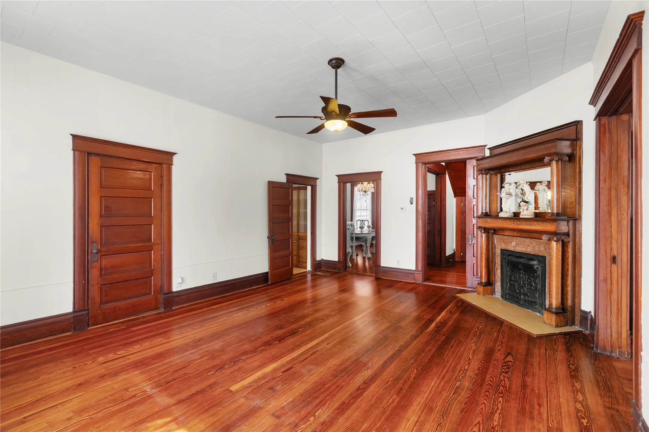 Hardwood flooring throughout, decorative fireplace with mantel, ceiling fan with integrated lighting, wood-paneled doors, and detailed wood trim