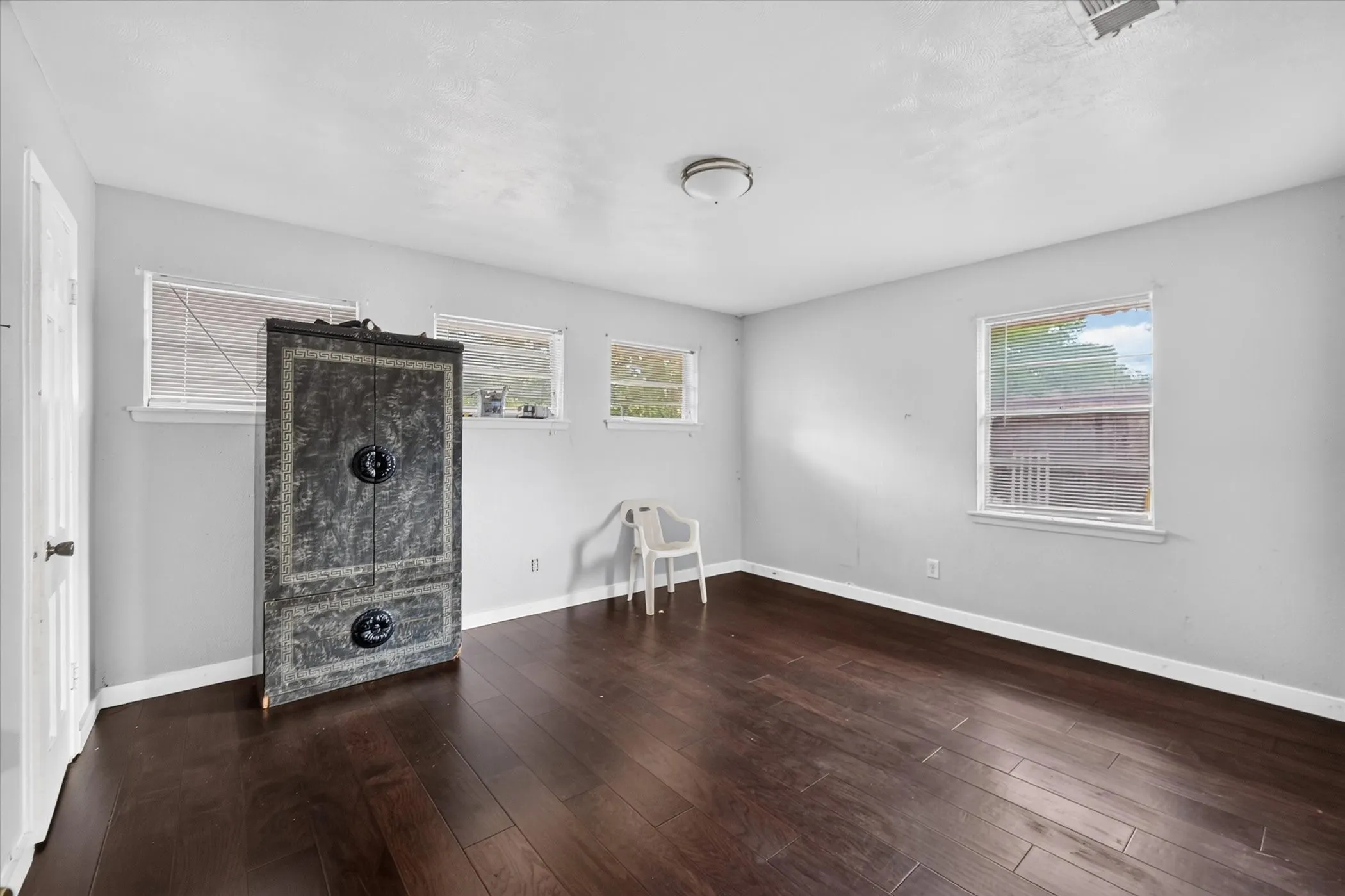 Dark wood-finish flooring with light gray walls, multiple windows, and a flush mount ceiling light fixture