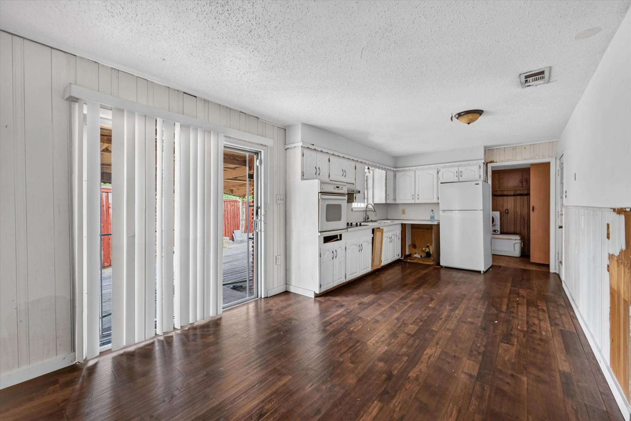 Wood-finish flooring, white cabinetry, a built-in oven, and a white refrigerator define this kitchen space