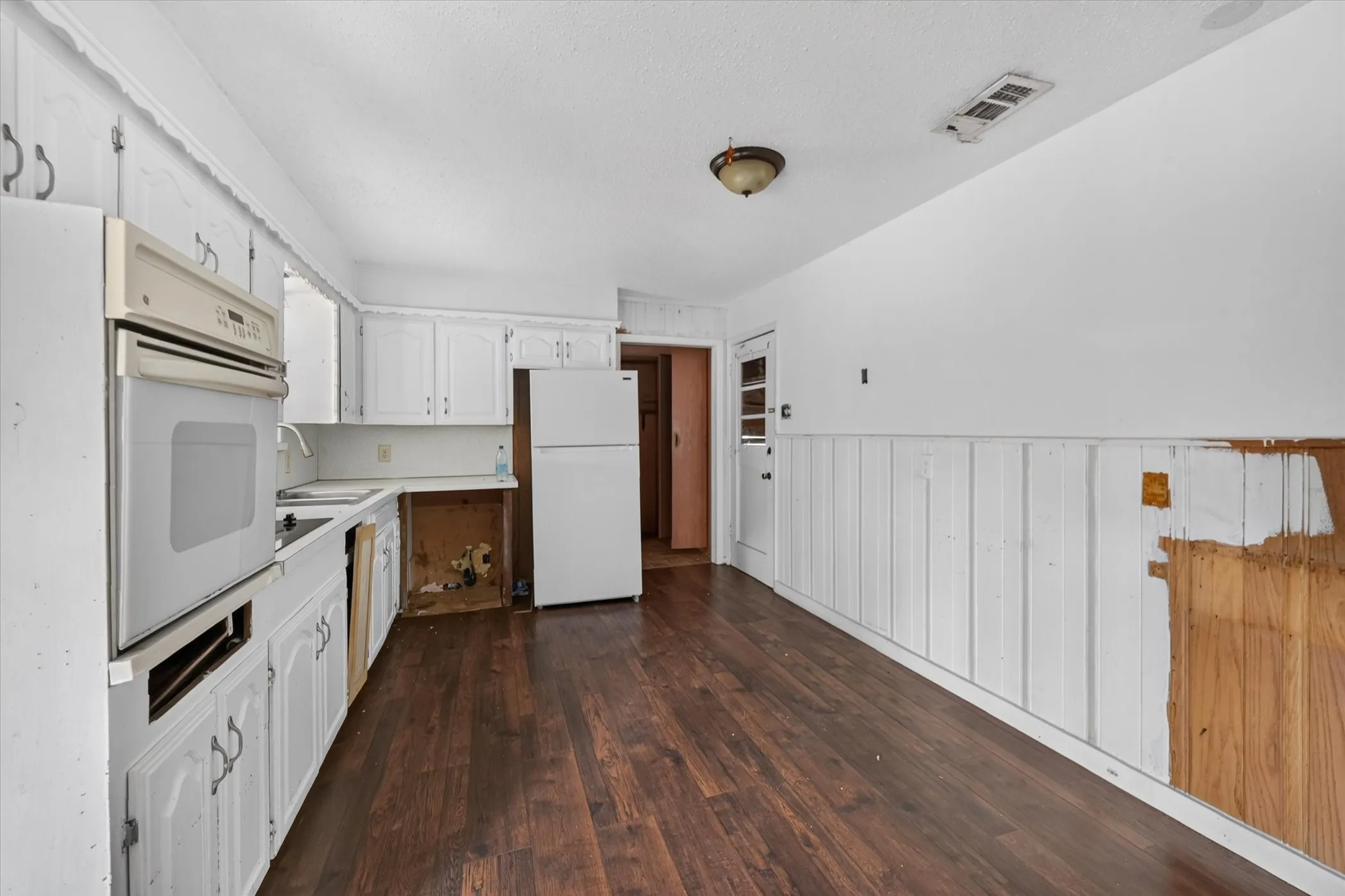 White cabinetry, wood-finish flooring, built-in oven, and a refrigerator