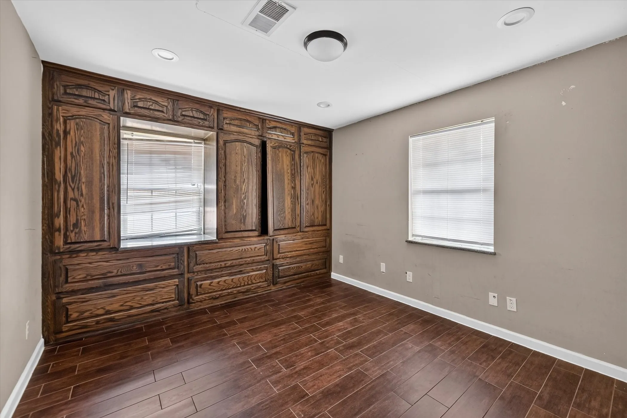 Wood-finish flooring, built-in dark wood cabinetry, recessed lighting, and a window with blinds