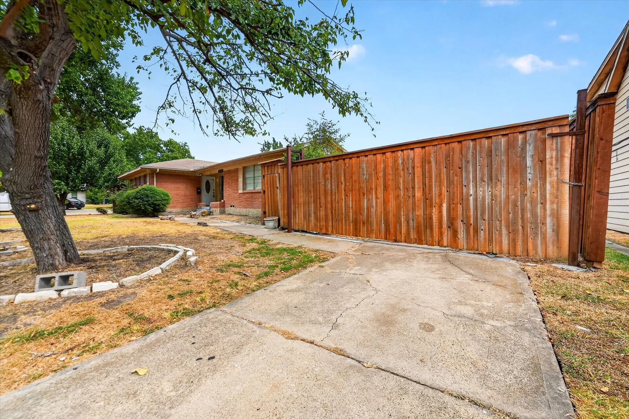 Red brick facade with a prominent wooden fence and concrete driveway