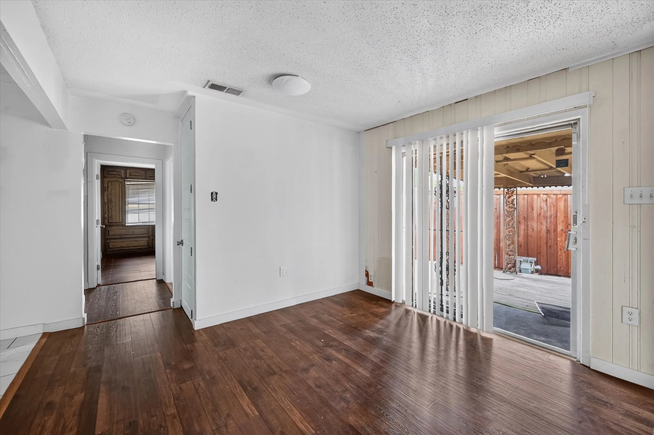 Hardwood-finish flooring, white painted walls, sliding glass door, and a textured ceiling