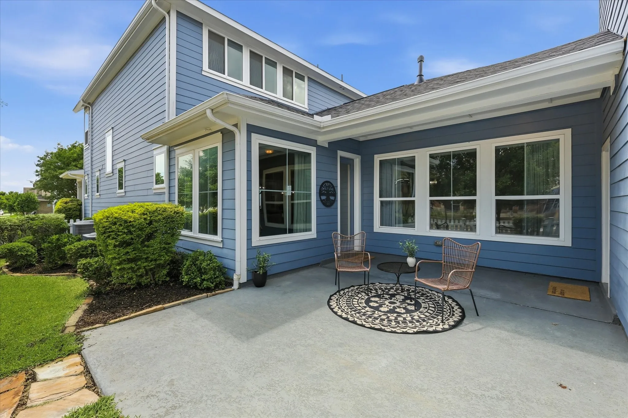 Spacious concrete patio with a covered overhang, surrounded by manicured landscaping and a grass lawn
