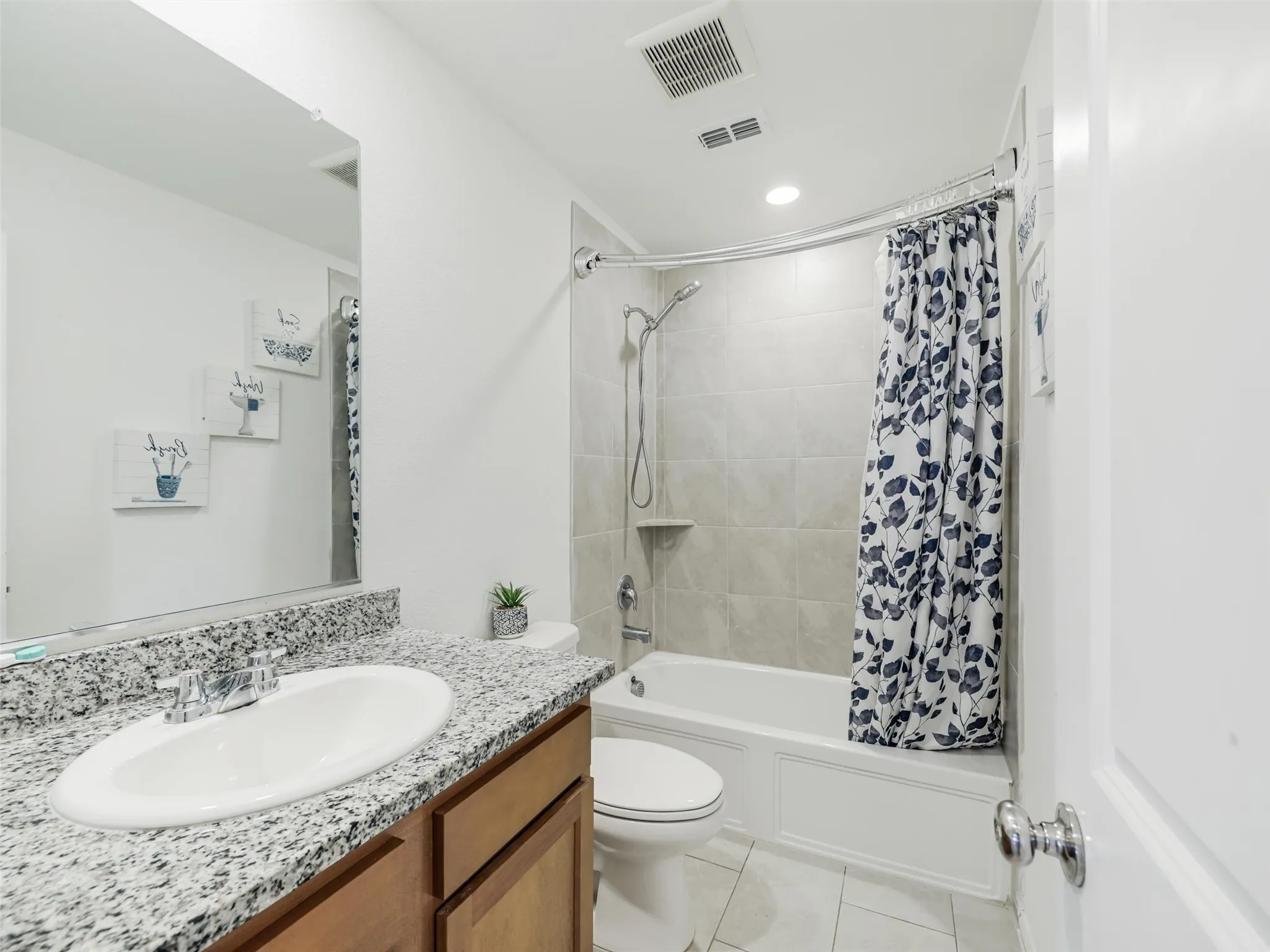 Granite-style countertop with an undermount sink, wood-finish vanity, and a tiled shower-bathtub combination