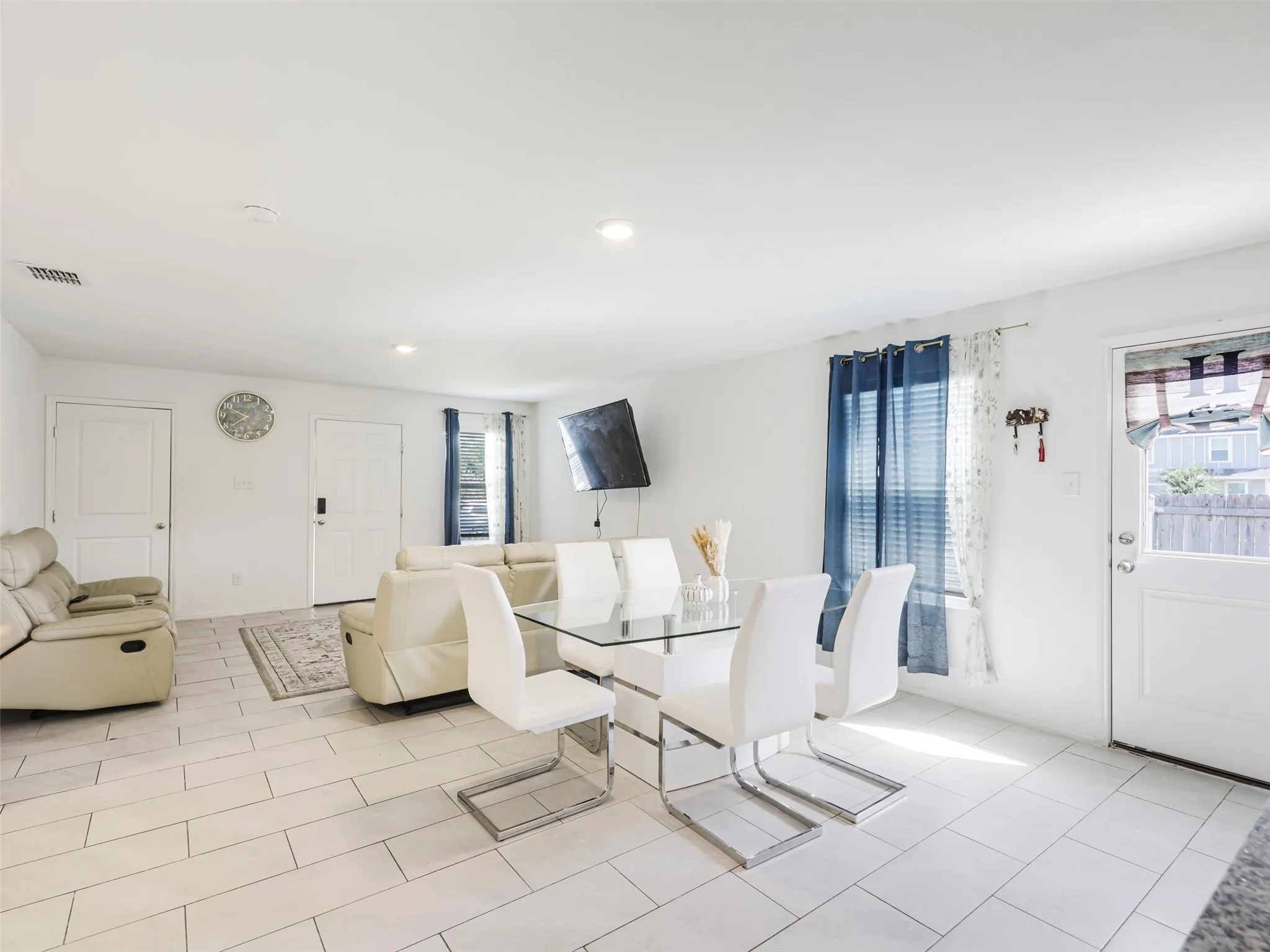 Open-concept living area with light-toned tiled flooring, white walls, and recessed lighting