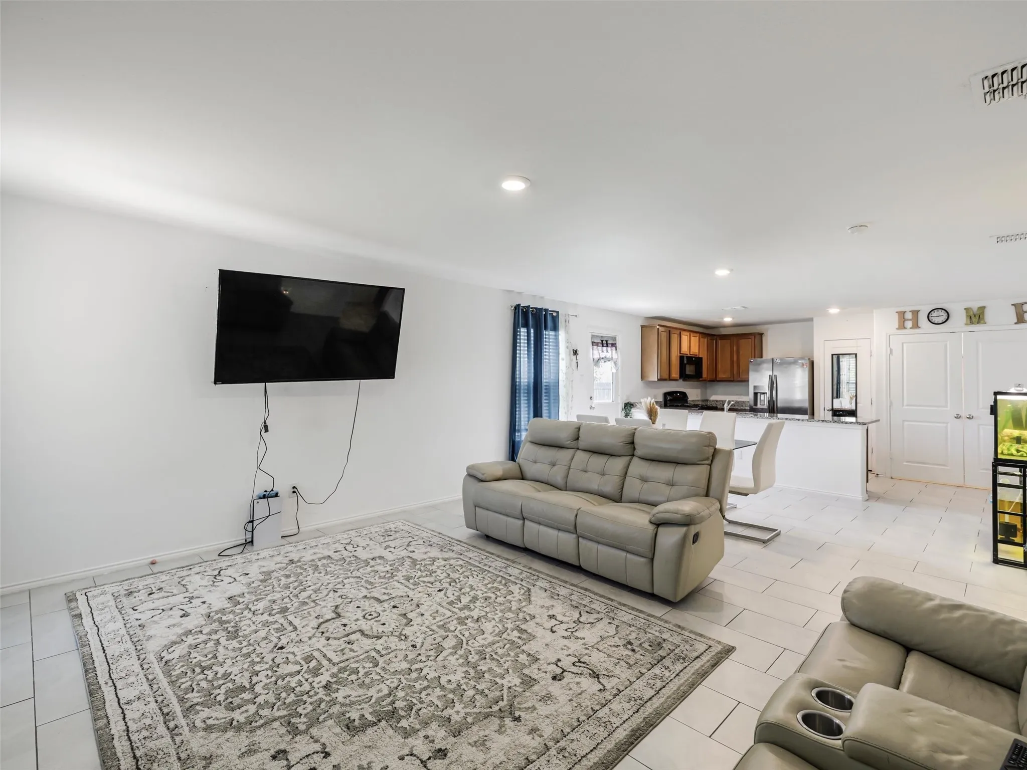 Open-concept living area featuring white tile flooring, recessed lighting, and a kitchen with wood cabinetry and stainless steel appliances