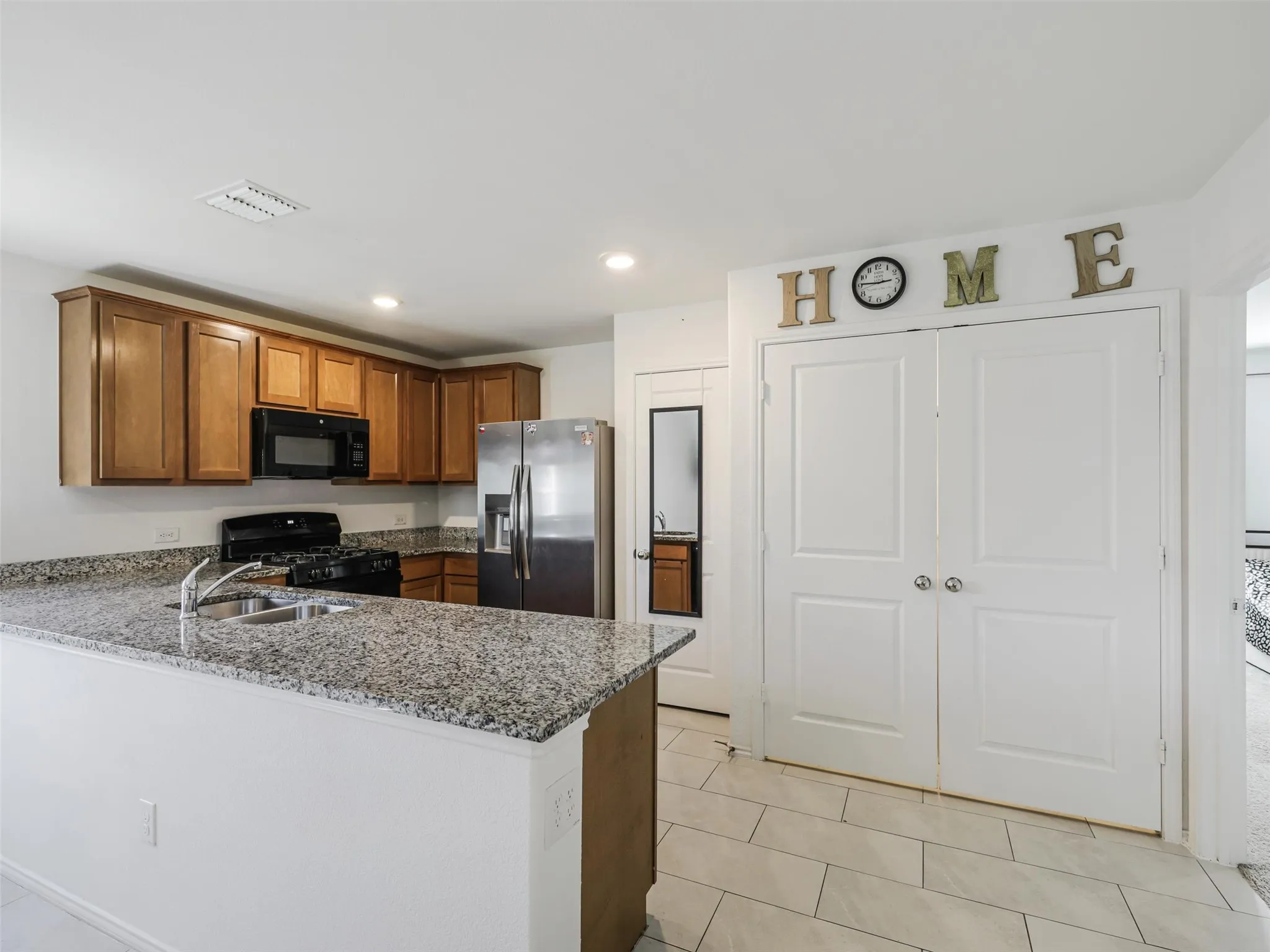 Kitchen featuring wood cabinetry, granite countertops, an undermount sink, stainless steel refrigerator, and tiled flooring