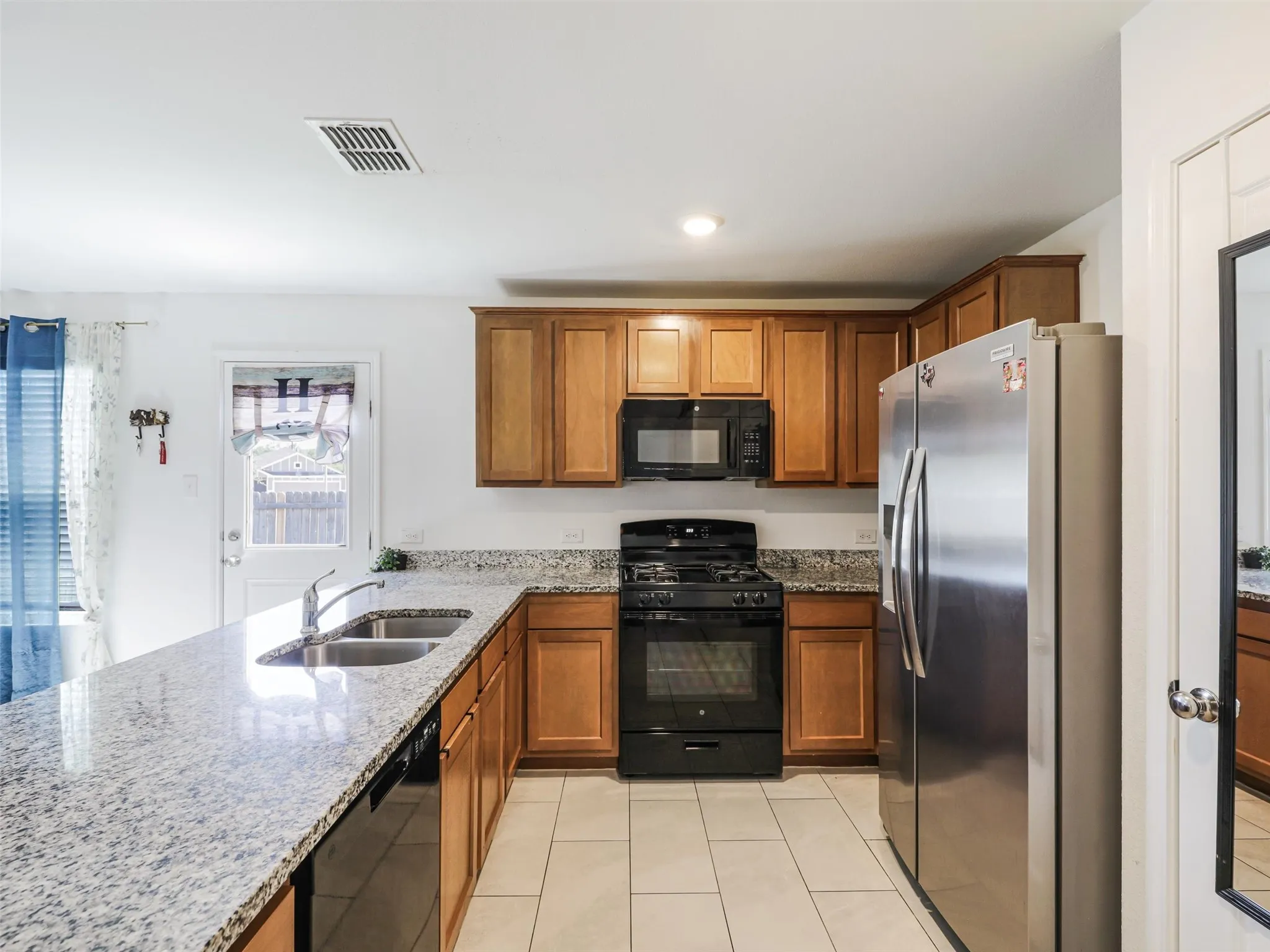 Kitchen featuring granite countertops, wood cabinetry, stainless steel refrigerator, black range, and tile flooring