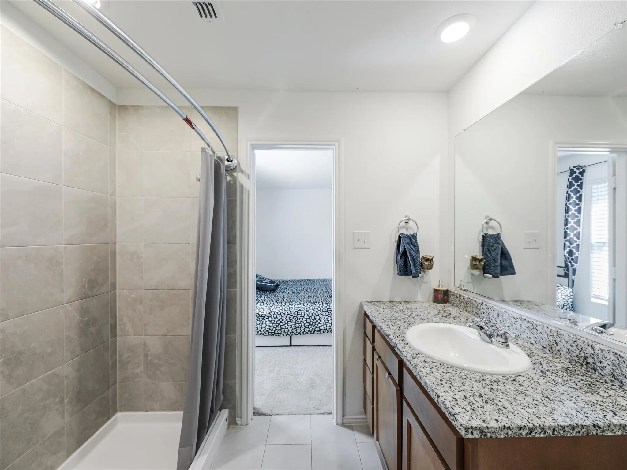 Bathroom featuring a tiled shower surround, recessed lighting, wood-finish vanity with an integrated sink, and a speckled countertop