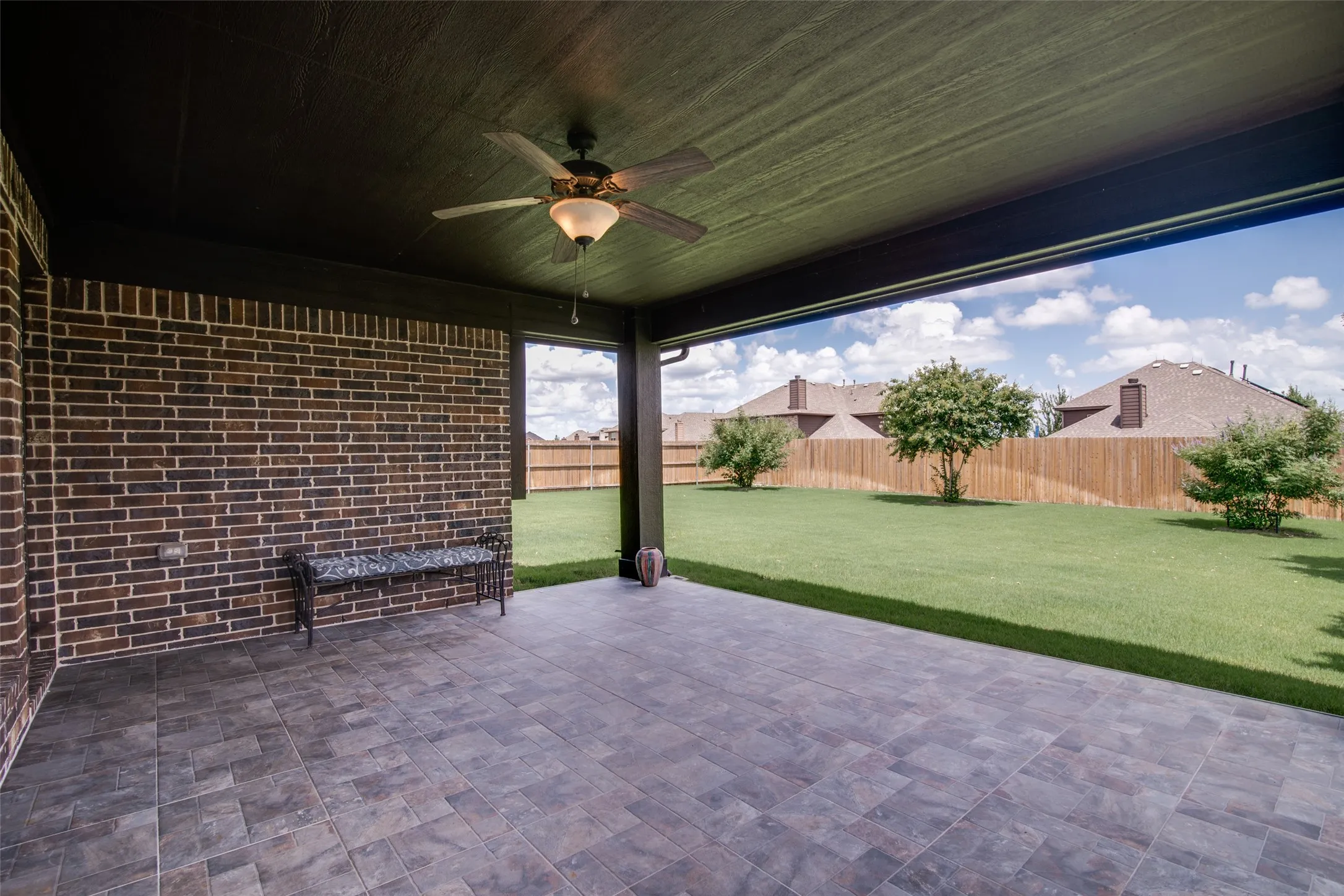 Covered patio featuring a ceiling fan, brick accent wall, and tile flooring