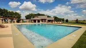 Expansive outdoor swimming pool with surrounding hardscaping, a nearby shaded pergola, and a stone-clad structure with a covered patio