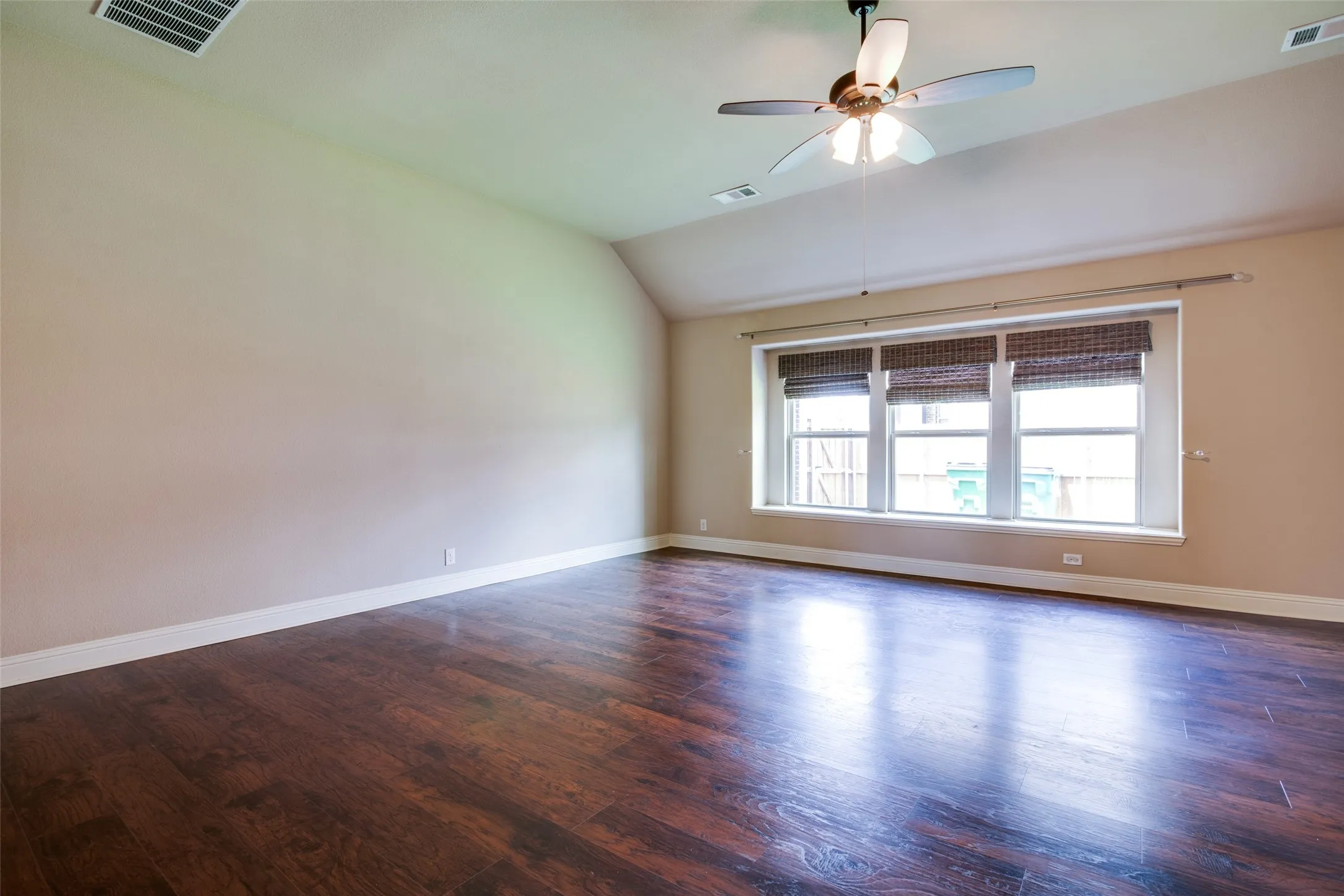 Expansive room featuring wood-finish flooring, multiple windows, a ceiling fan with integrated lighting, and a neutral wall color
