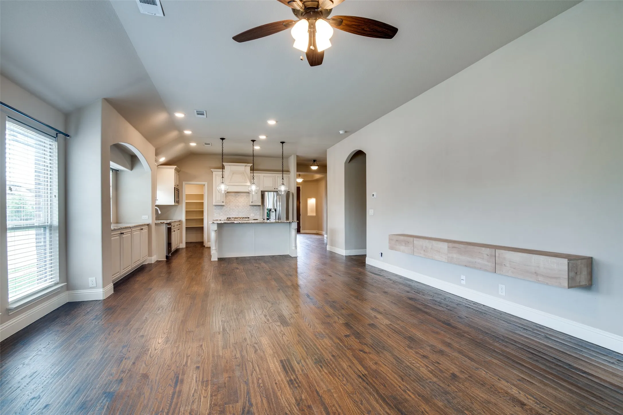 Open-concept living area showcasing rich wood-finish flooring, recessed lighting, and a ceiling fan with integrated light fixture