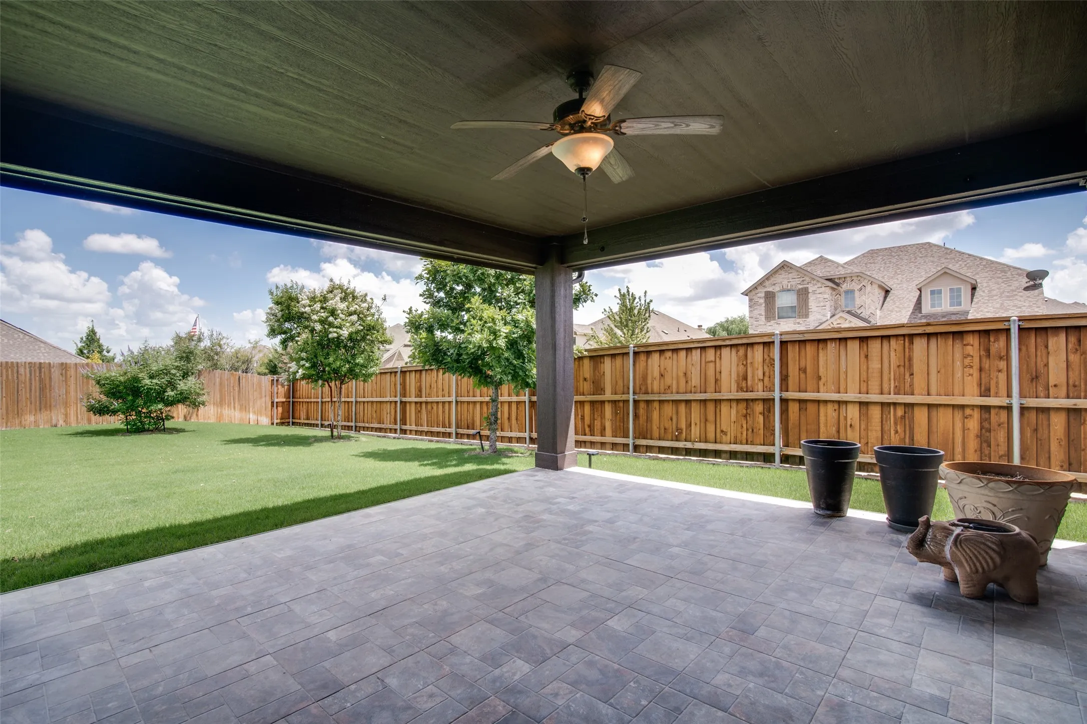 Covered patio featuring a ceiling fan with integrated lighting, paver flooring, and a manicured lawn