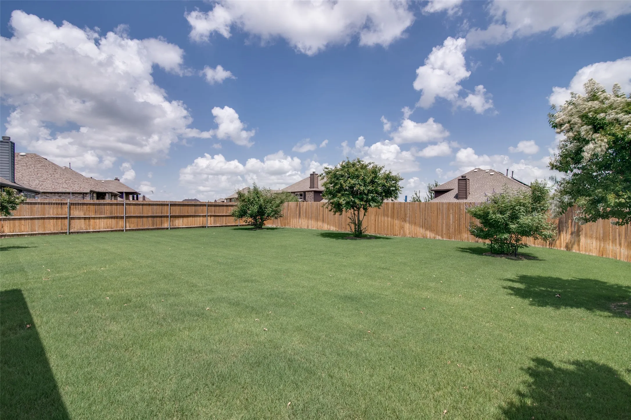 Expansive backyard with a lush lawn, privacy fencing, and mature trees
