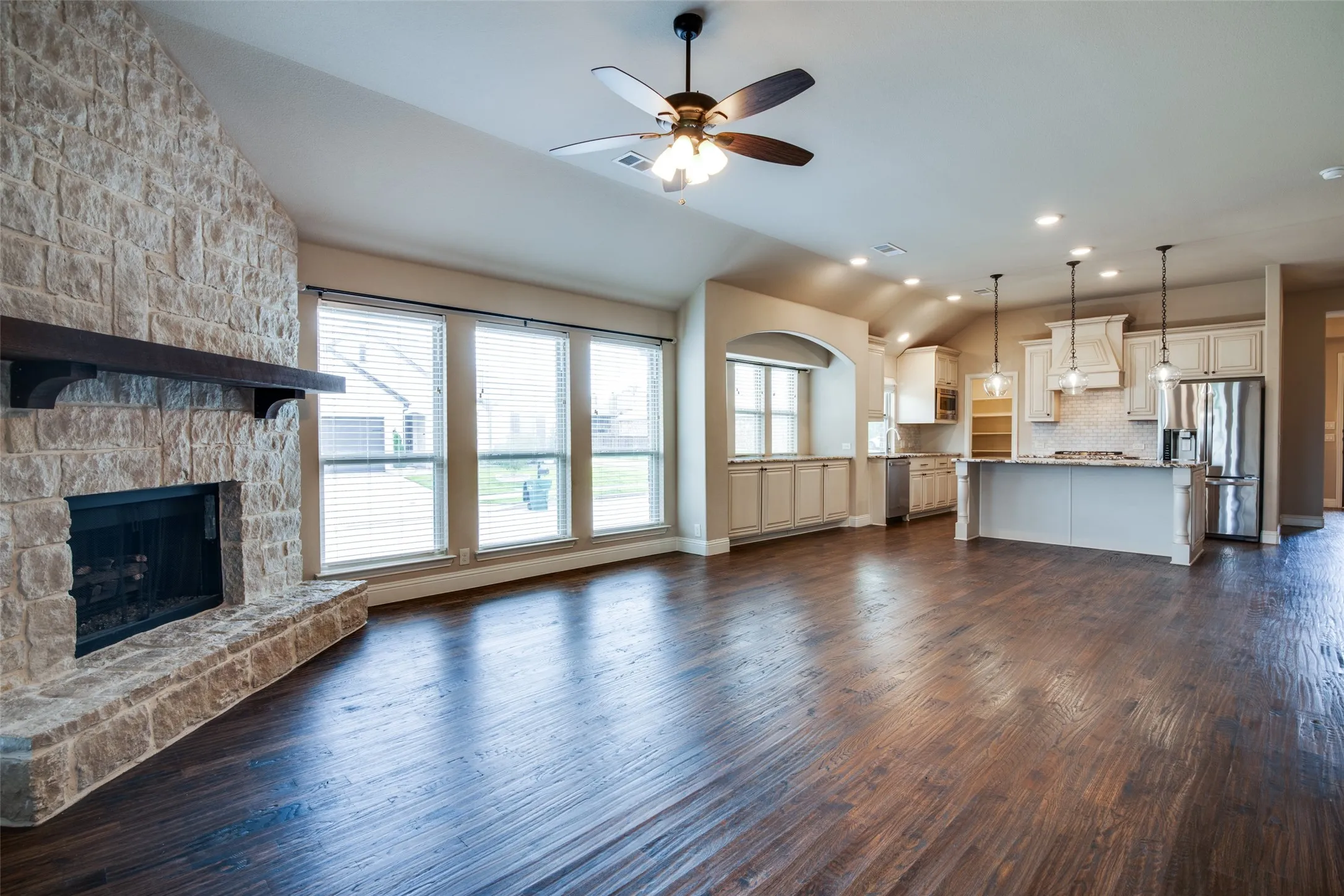 Open-concept living space featuring hardwood flooring throughout, a stone fireplace with black surround, and abundant natural light from multi-pane French doors and windows