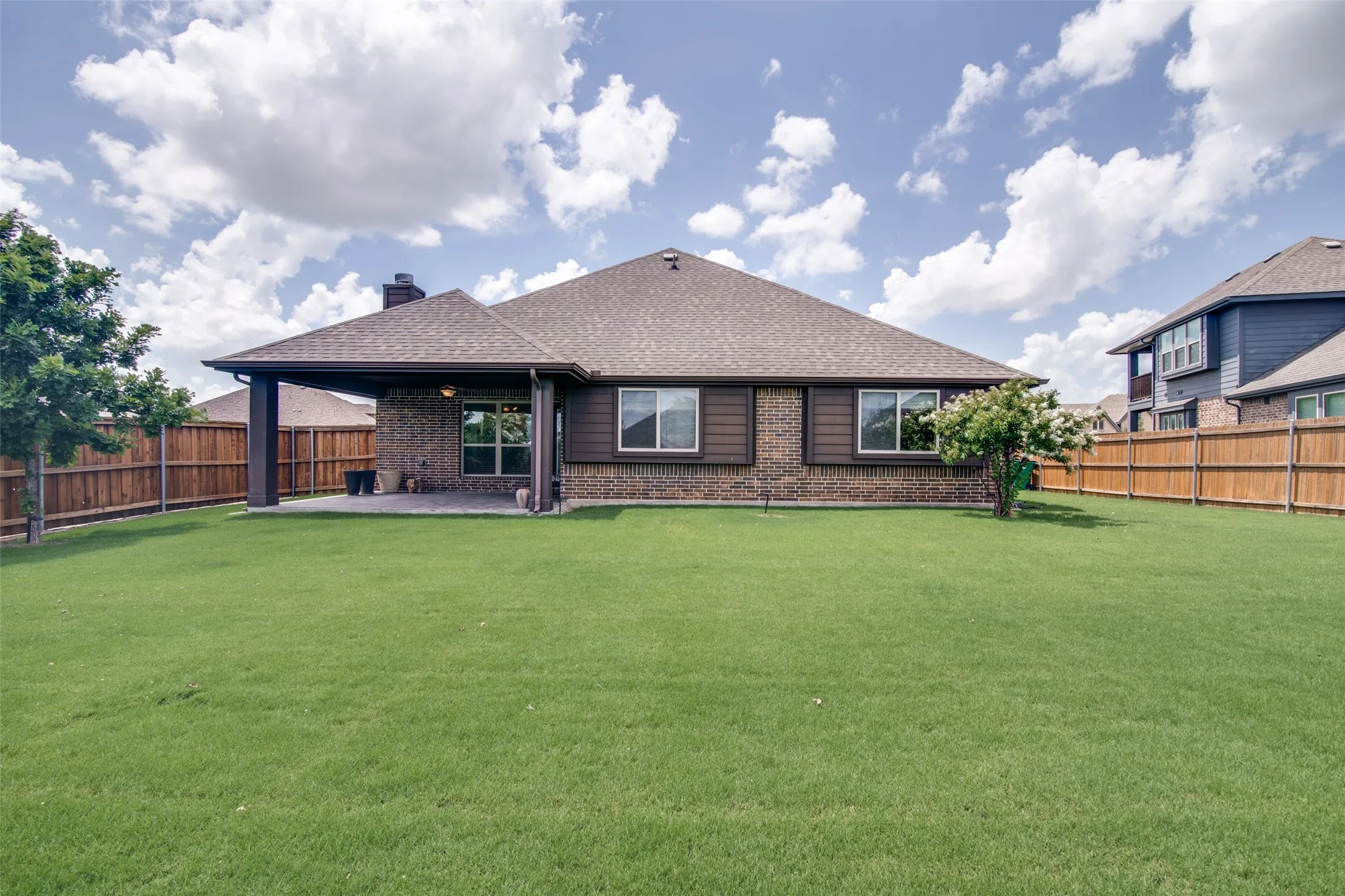 Expansive backyard featuring a manicured lawn, full privacy fencing, and a covered patio