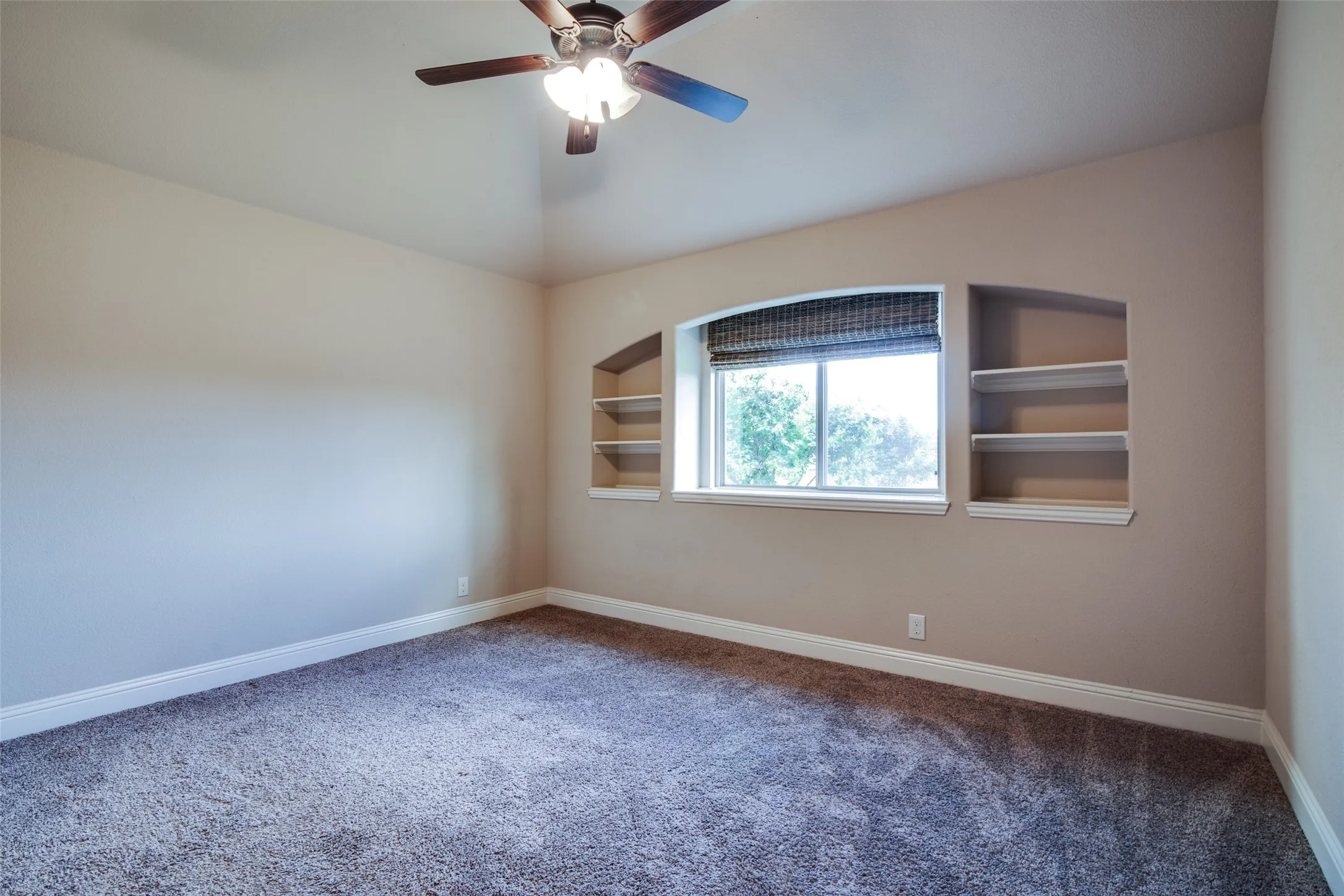 Recessed window with arched detail, built-in shelving, ceiling fan with integrated lighting, and wall-to-wall carpeting