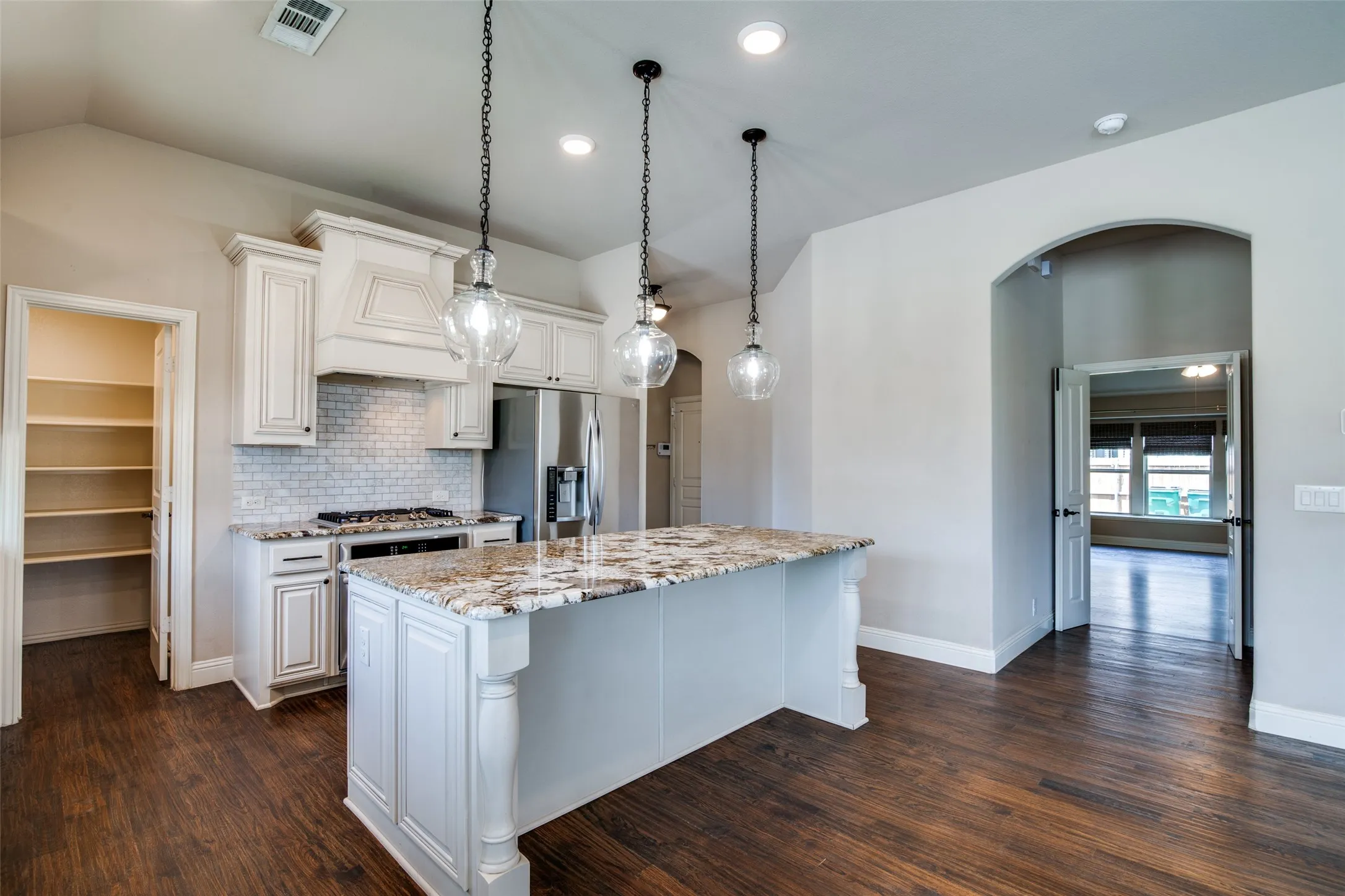 Gourmet kitchen featuring a large central island with a stone-finish countertop, white cabinetry, integrated stainless-steel appliances, and a tiled backsplash