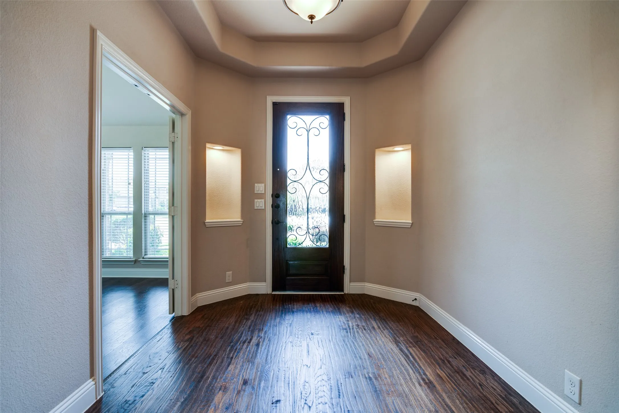 Entryway featuring wood-finish flooring, a decorative glass-paneled entry door, recessed wall niches, crown molding, and a tray ceiling