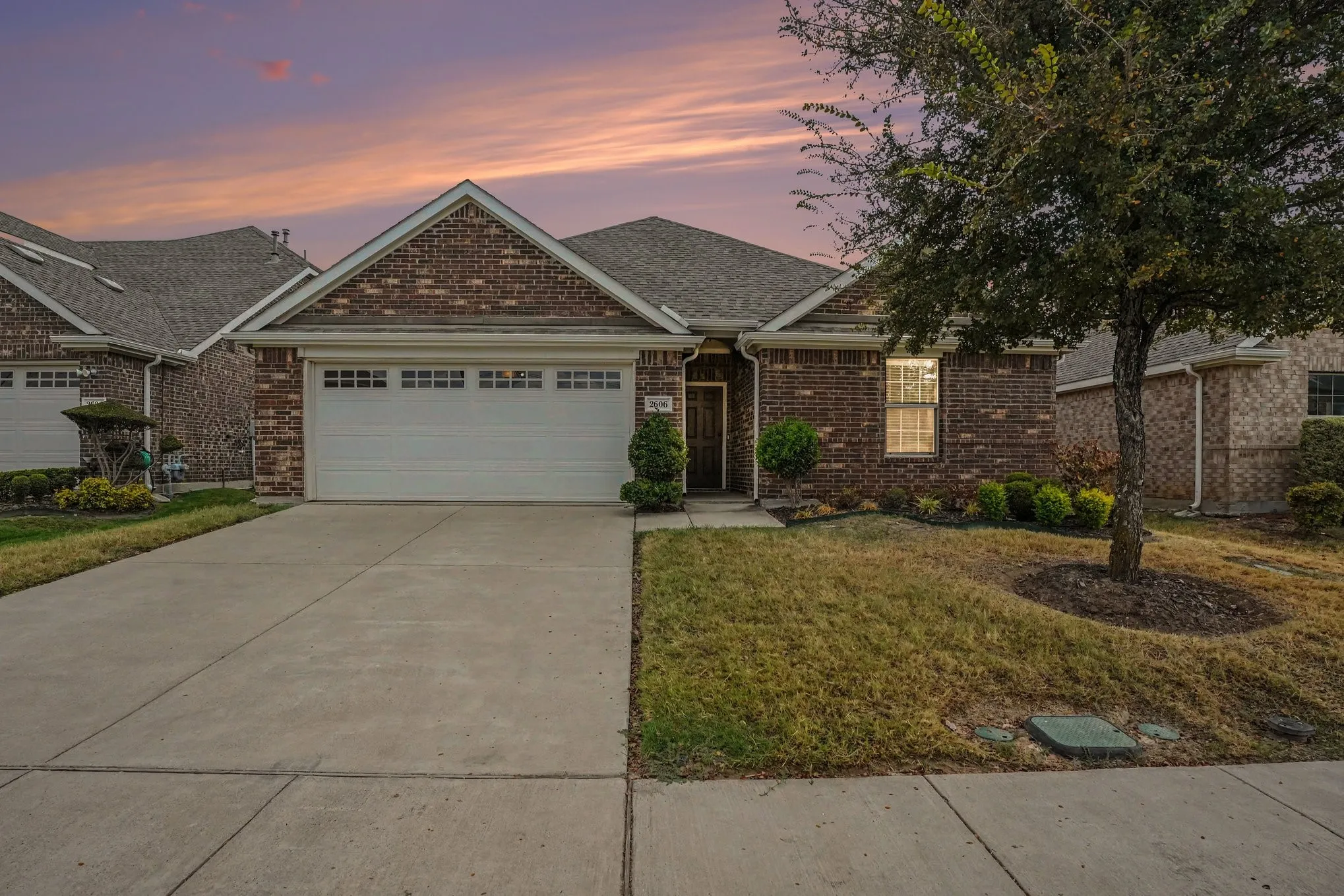 Brick exterior with a gabled roofline, attached garage, concrete driveway, and mature landscaping