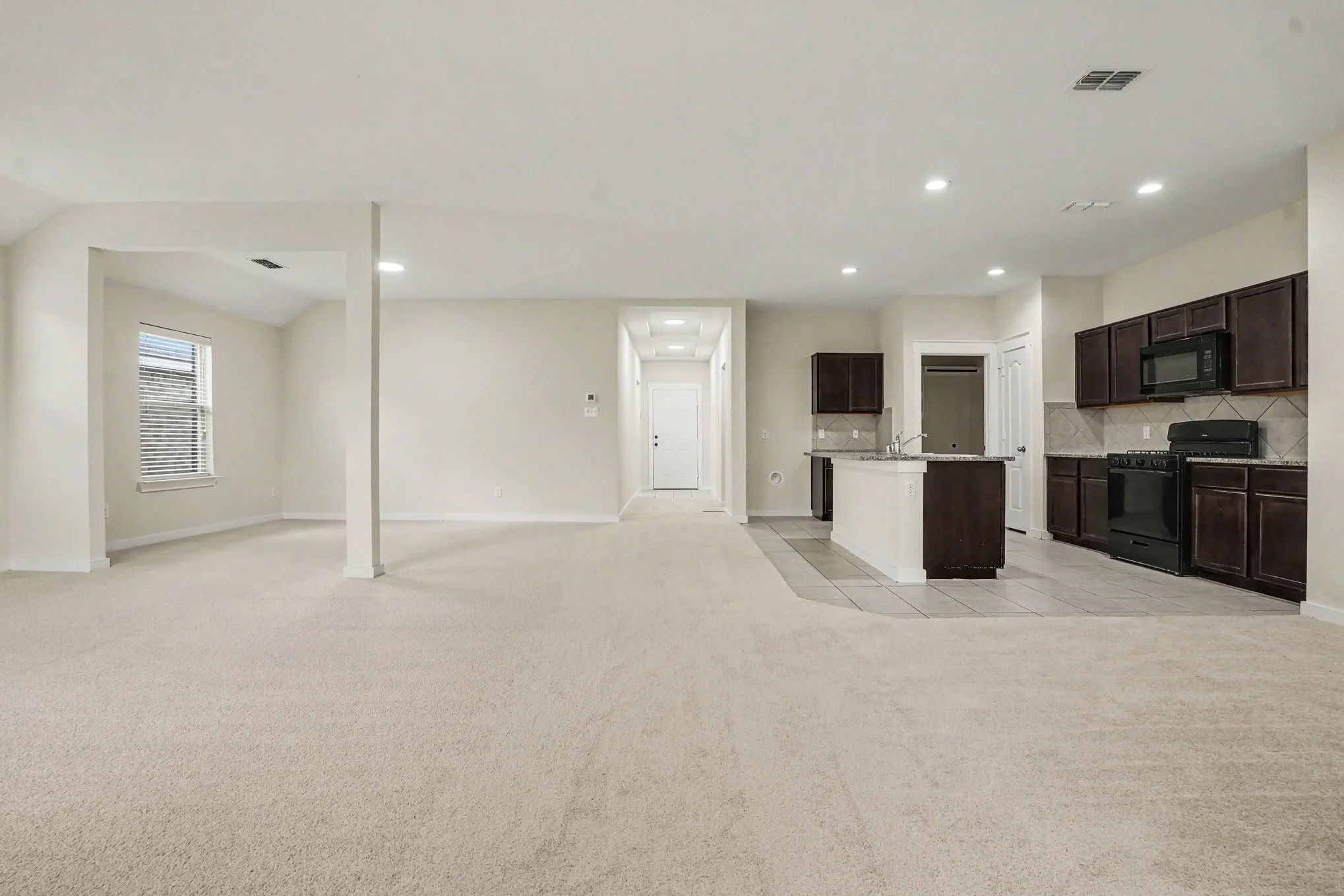 Open-concept living area with light-toned carpeting, recessed lighting, and a window with horizontal blinds