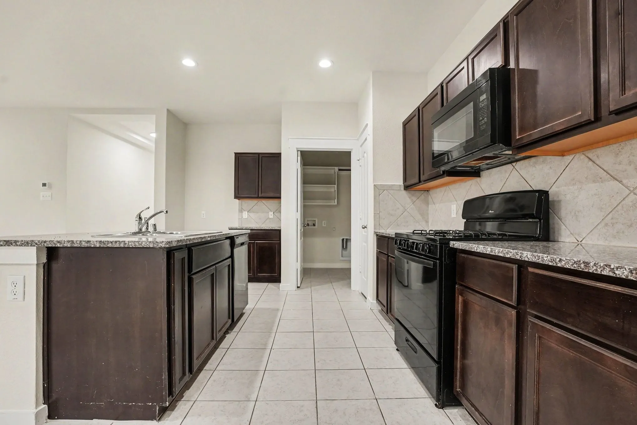 Kitchen featuring dark wood-finish cabinetry, light stone-finish countertops, tile flooring, and a tile backsplash