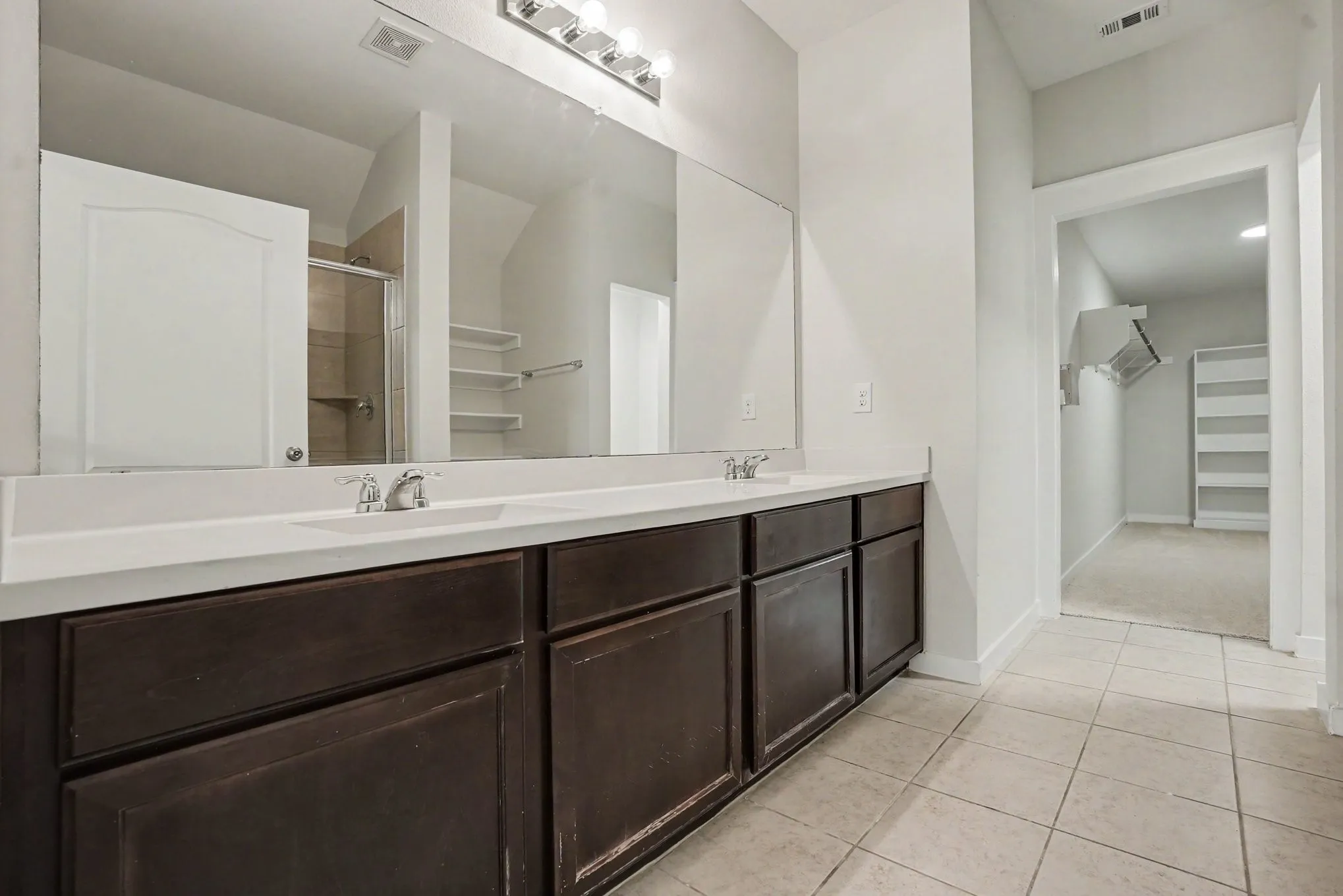 Master- Dual vanity with integrated sinks, expansive mirror, dark wood-finish cabinetry, and tiled flooring