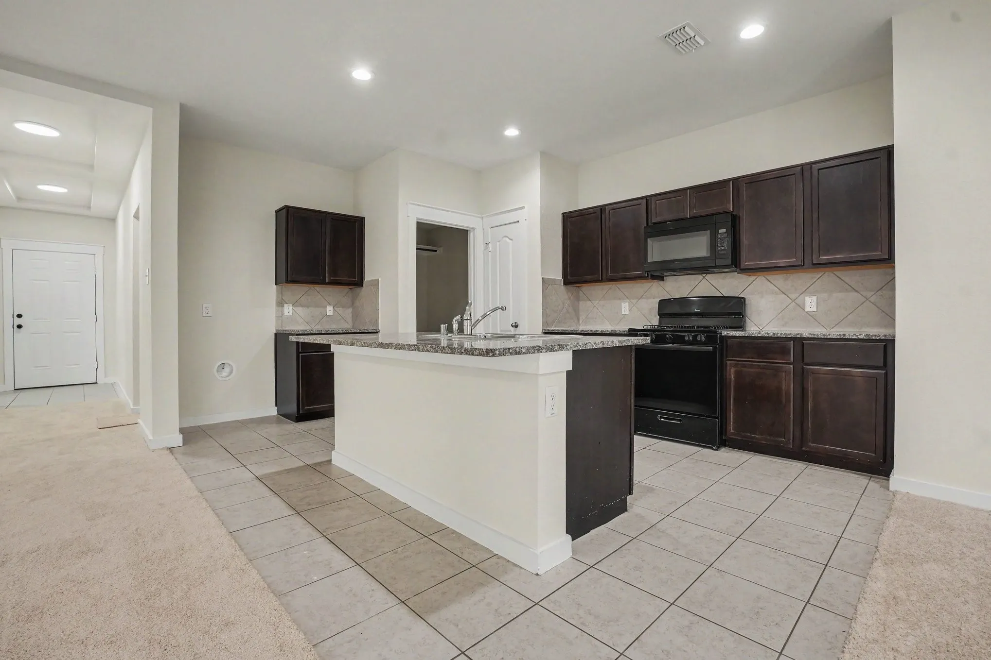 Kitchen featuring a central island with countertop, dark wood-finish cabinetry, tile flooring, and integrated black appliances