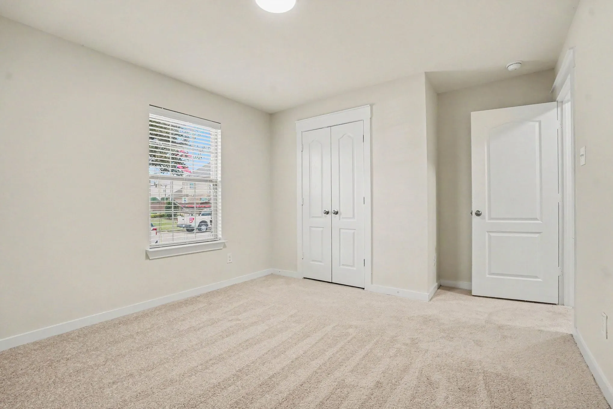 Bedroom 2- Neutral carpet flooring, a window with blinds, a built-in closet with double doors, and a flush-mount ceiling light fixture
