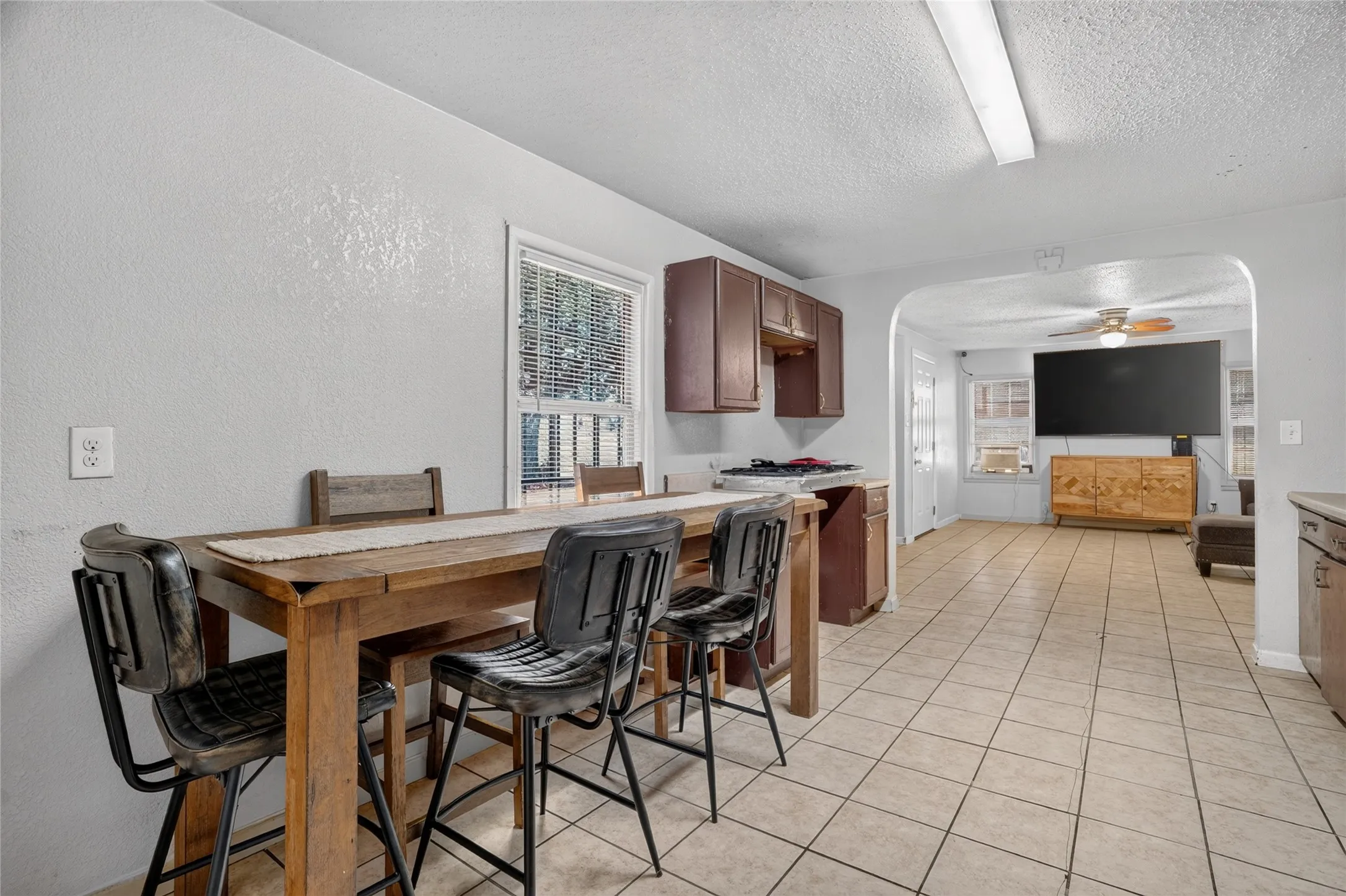 Kitchen and dining area featuring tile flooring, a window with blinds, and wood-finish cabinetry
