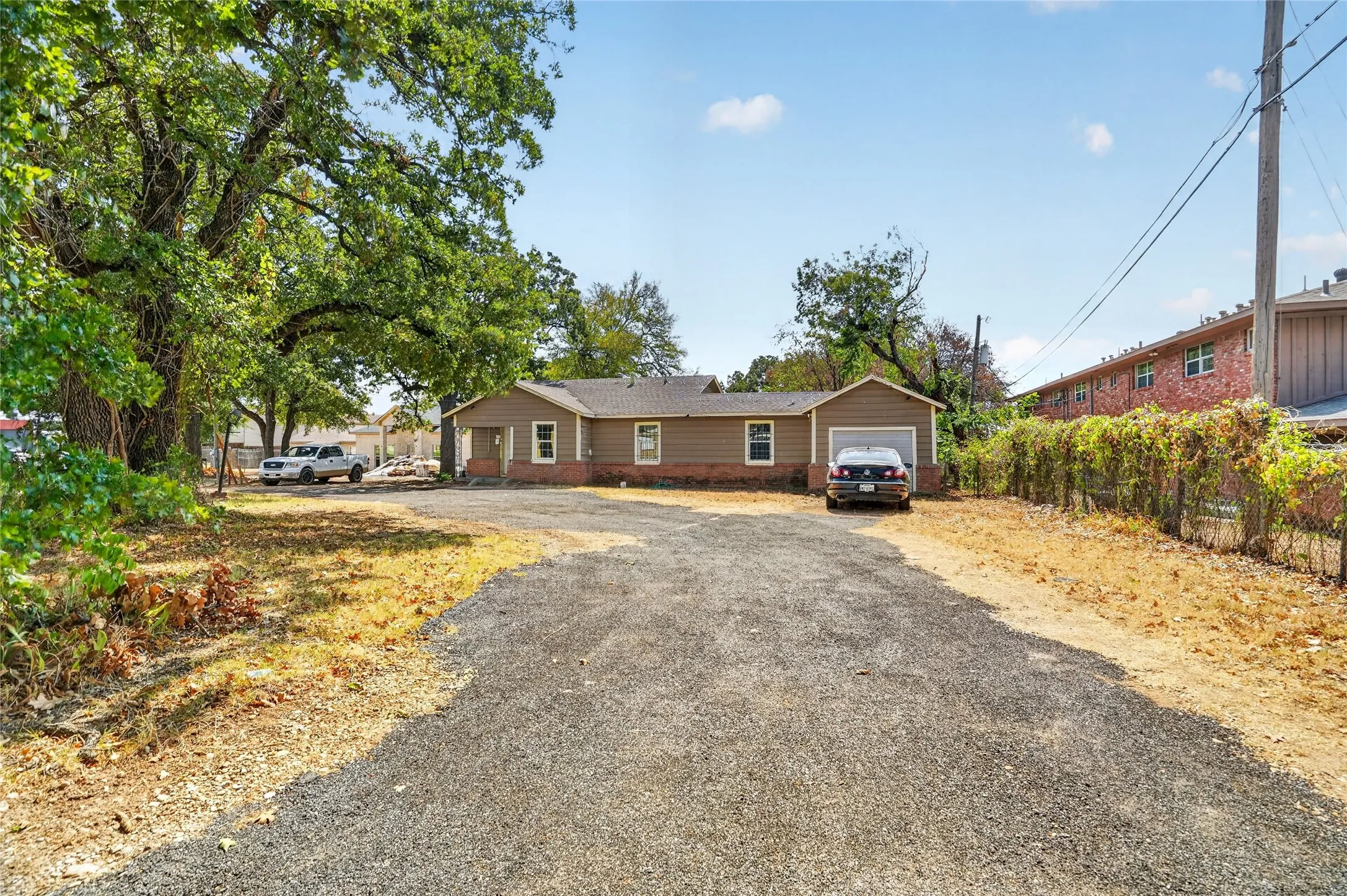Single-story residence featuring a gravel driveway, attached garage, and mature trees