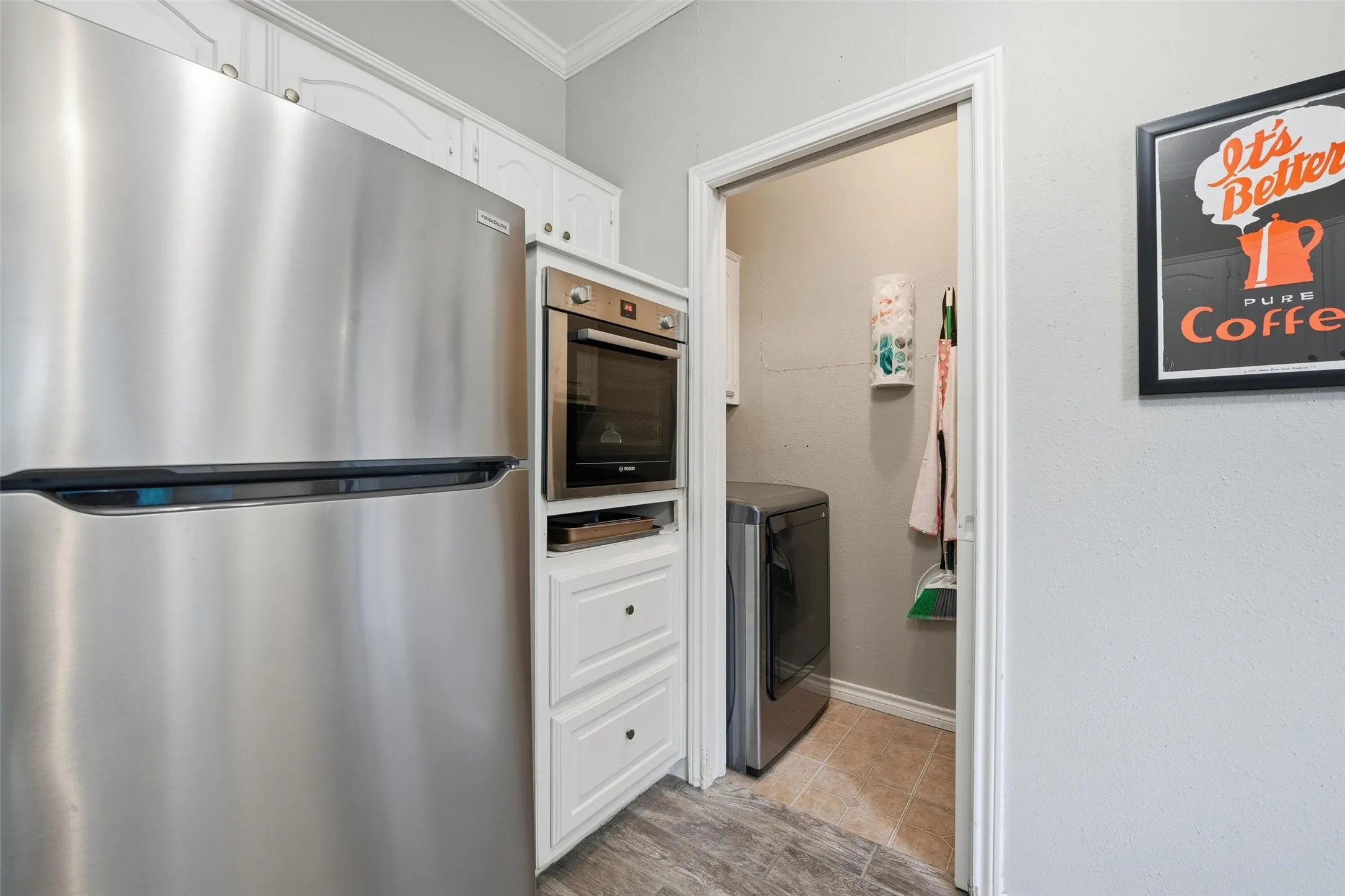 Stainless steel refrigerator, built-in oven, white cabinetry, wood-finish flooring, and a laundry area with a washing machine