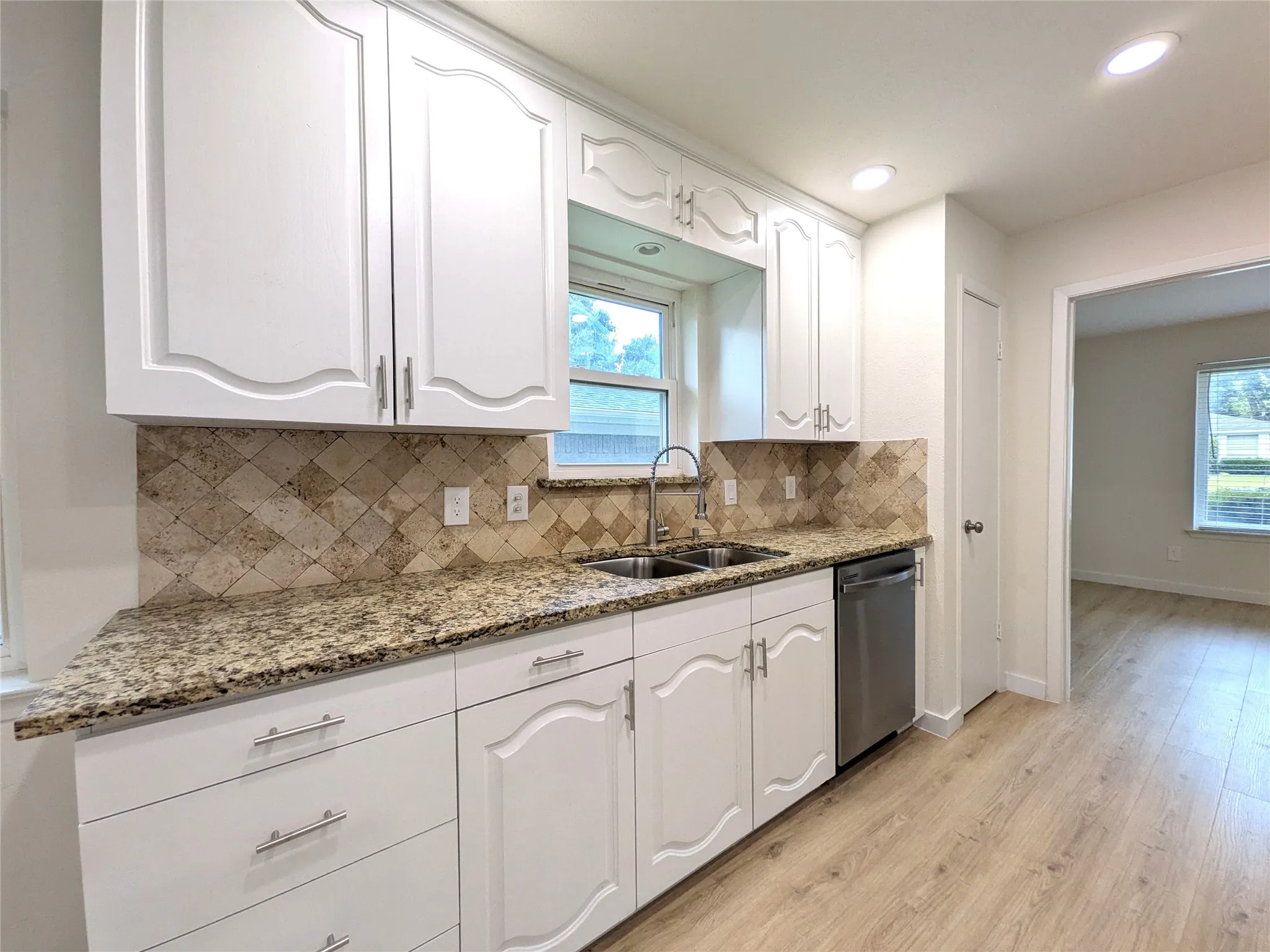Kitchen featuring white cabinetry, granite countertops, a stainless steel sink, a tile backsplash, and light wood-finish flooring