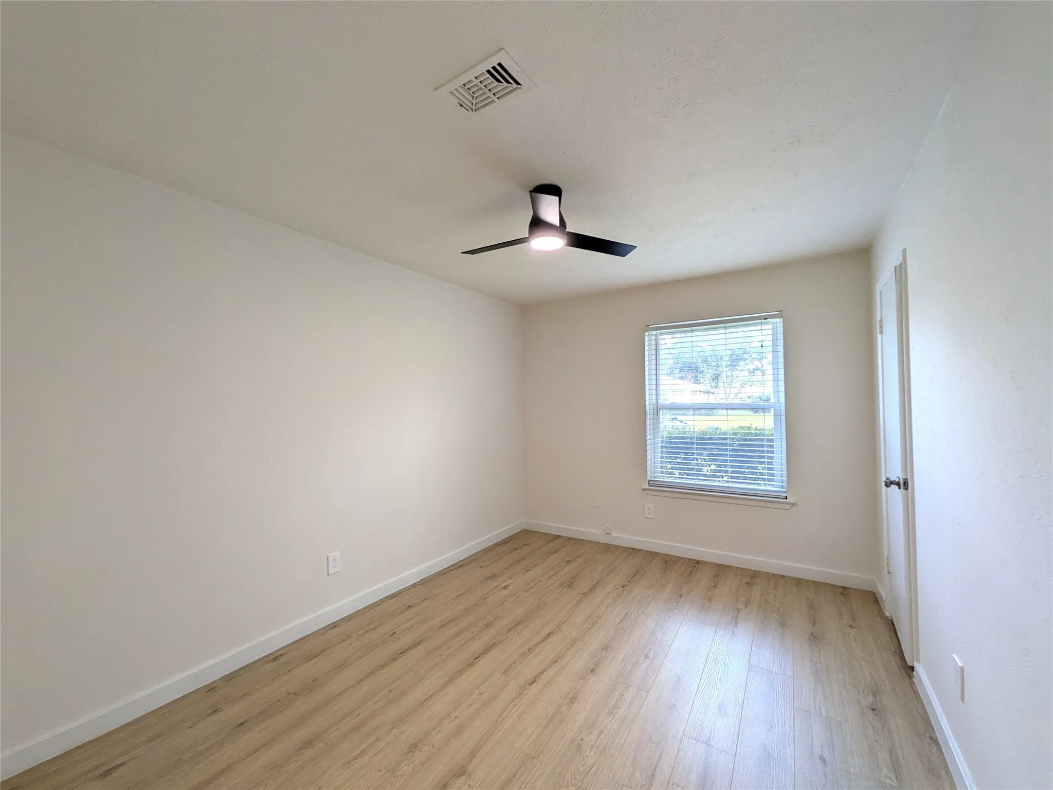 Bright interior space featuring wood-finish flooring, a modern ceiling fan with integrated lighting, and a single window with horizontal blinds