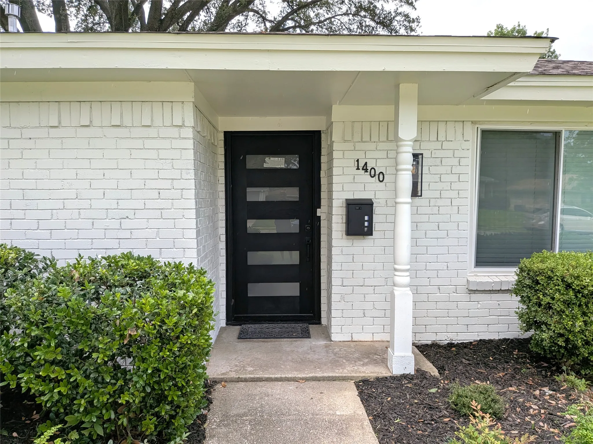 White painted brick exterior with a modern black entry door featuring horizontal glass panels
