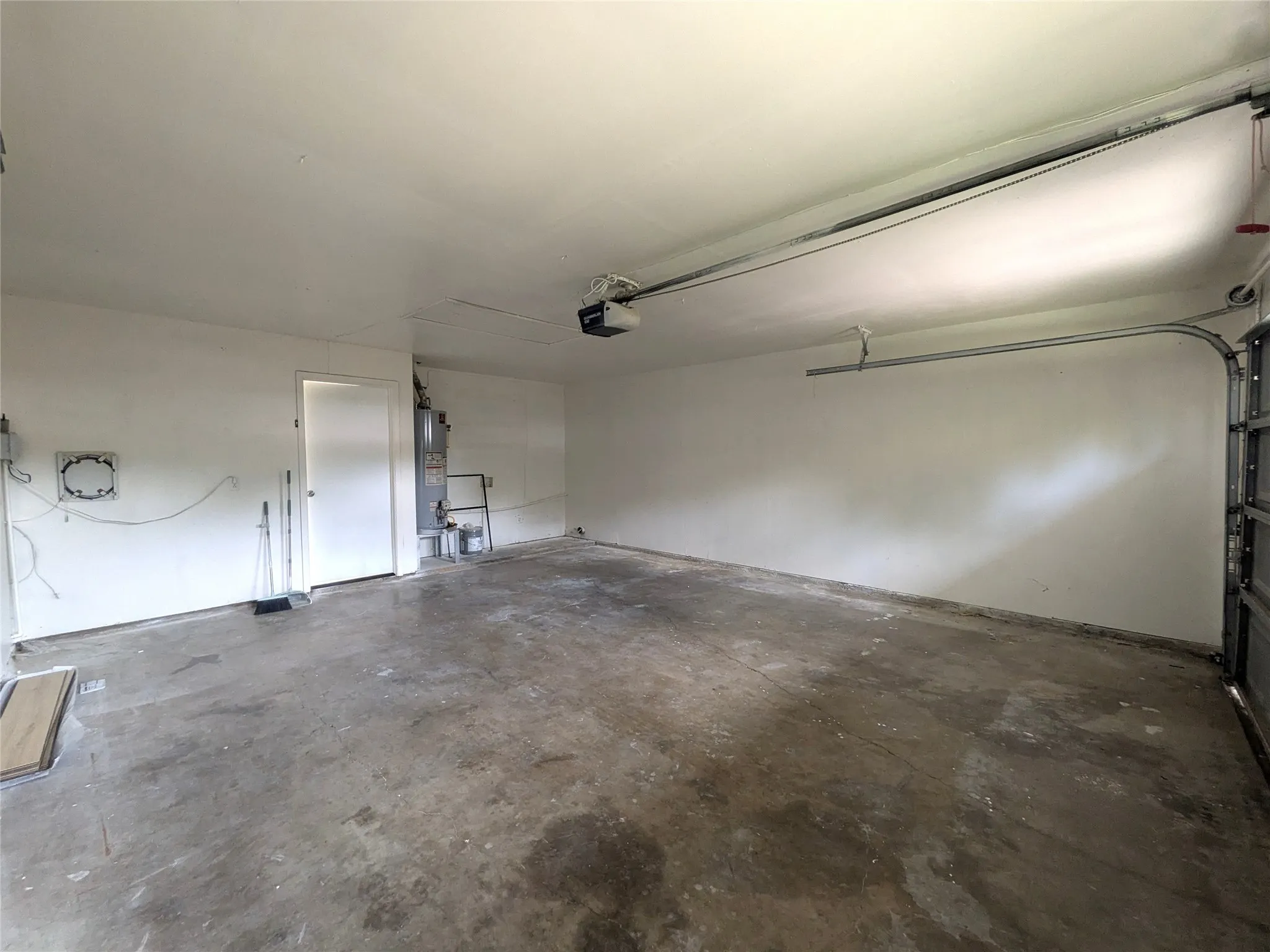 Spacious garage with an overhead door opener, concrete flooring, and a white interior door