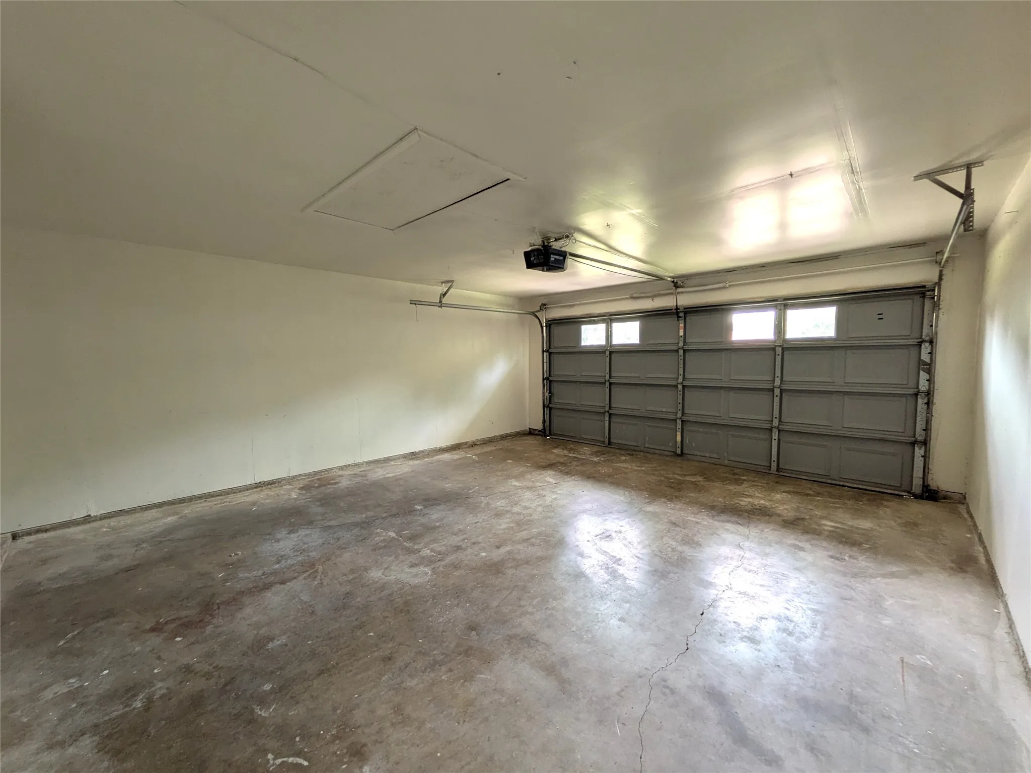 Interior garage space featuring a grey sectional garage door with upper window inserts, an automatic garage door opener, and a ceiling access panel