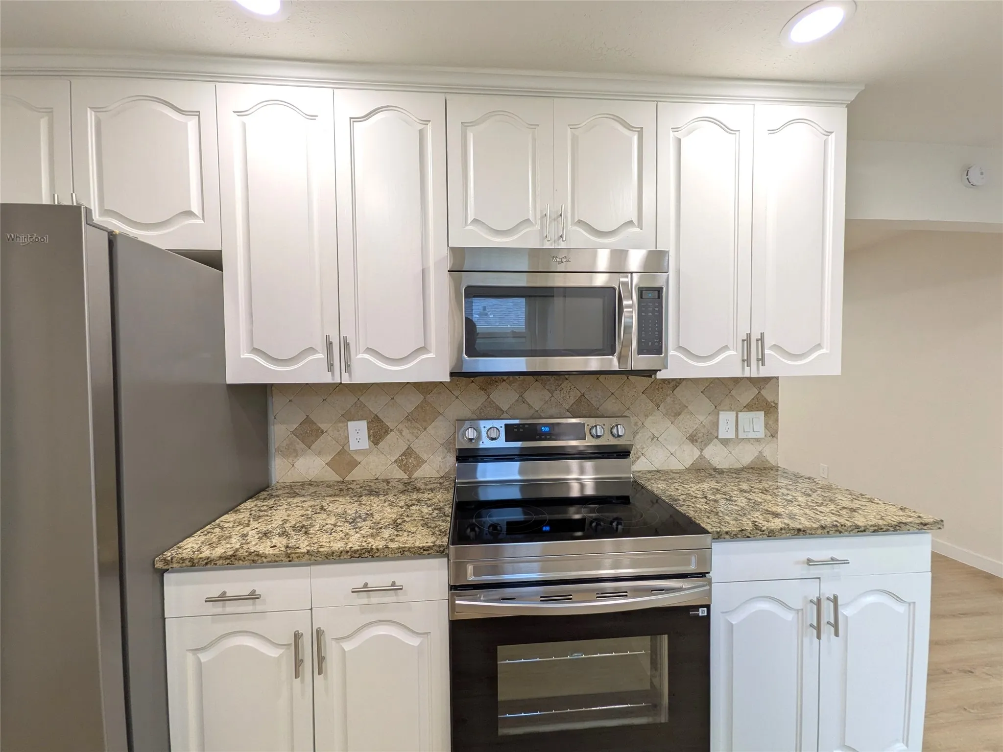 Kitchen featuring white cabinetry with brushed nickel hardware, stainless steel appliances, granite countertops, and a mosaic tile backsplash
