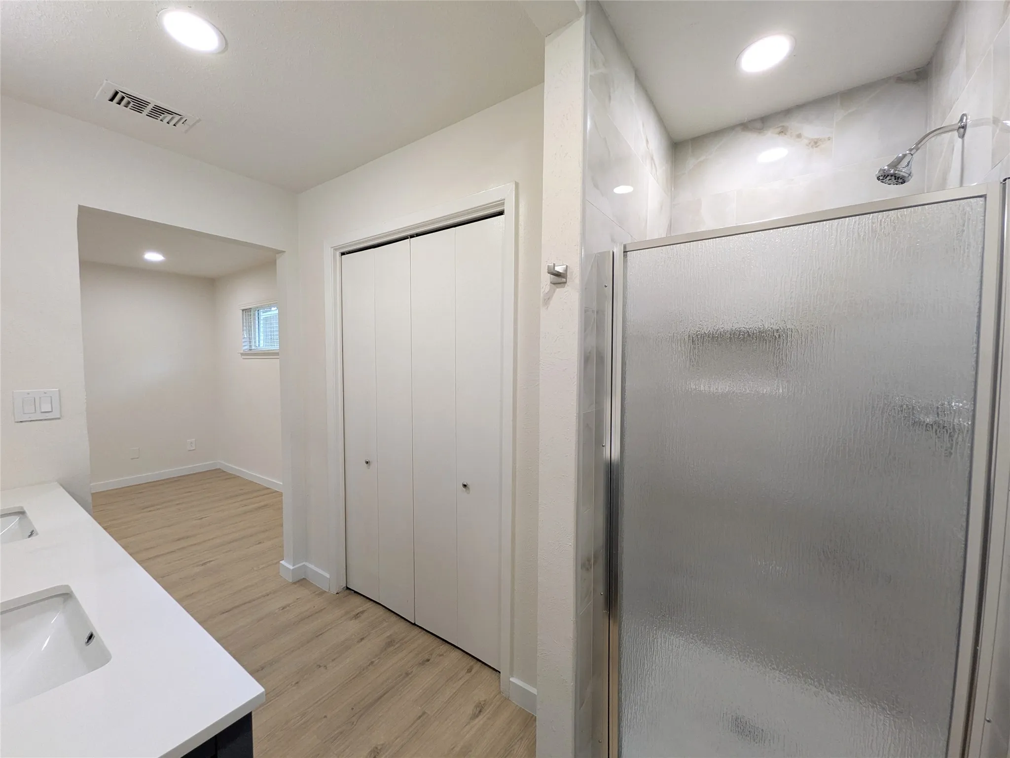 Spacious bathroom featuring a glass-enclosed shower with tiled walls, a dual-sink vanity with white countertops, bi-fold closet doors, and recessed lighting