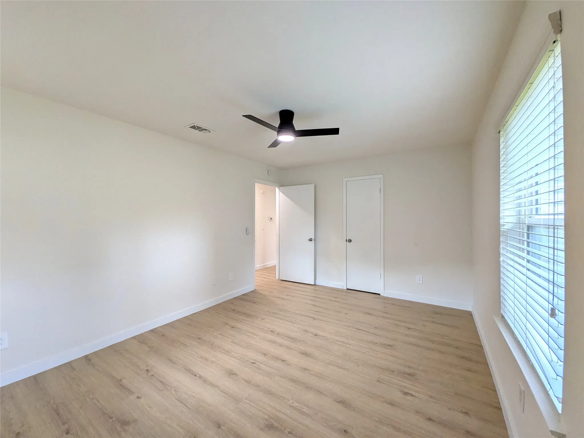 Spacious interior room featuring wood-finish flooring, a contemporary ceiling fan, and white baseboards