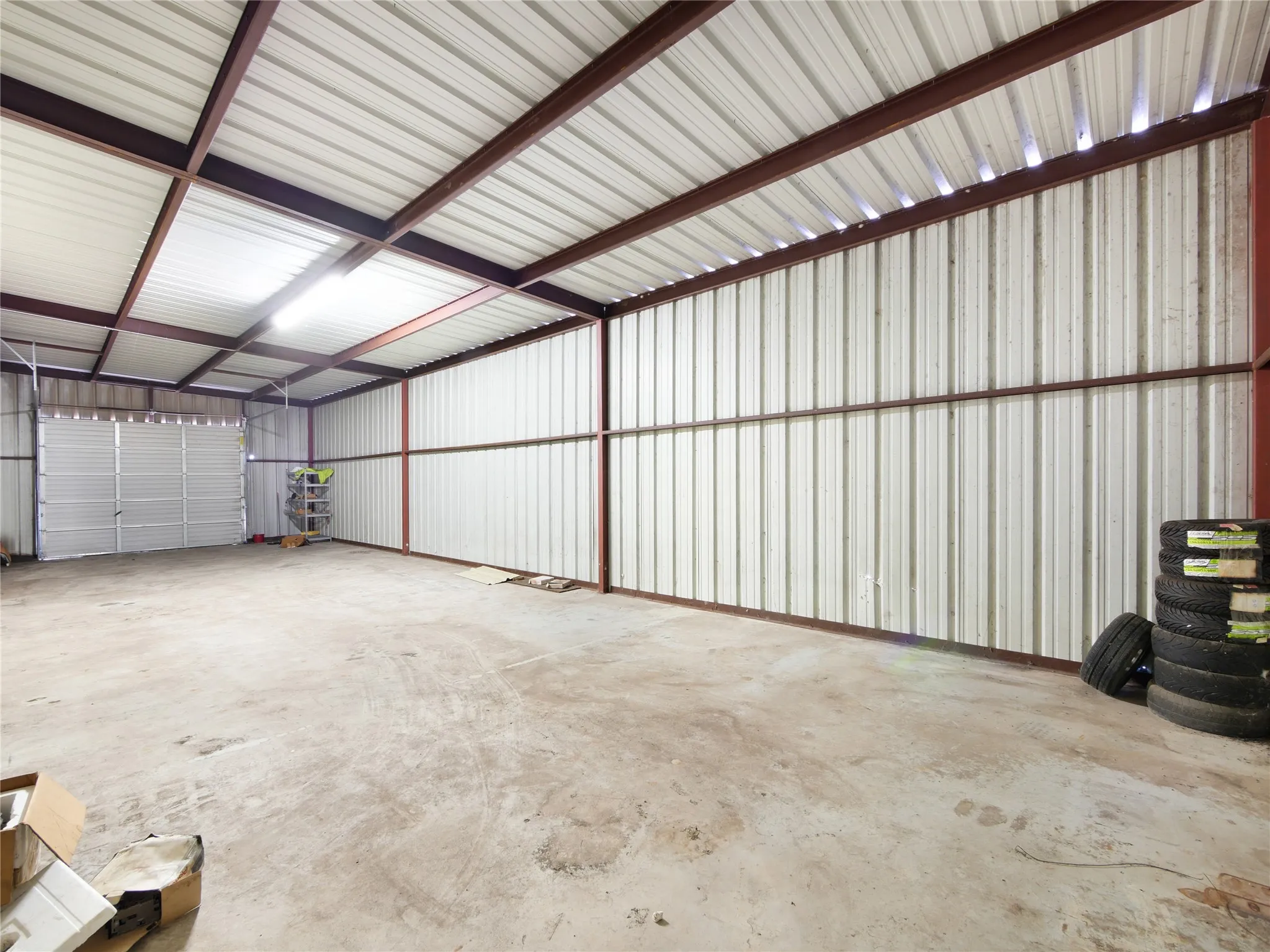 Expansive interior featuring a concrete floor, corrugated metal walls, exposed structural beams, and overhead lighting