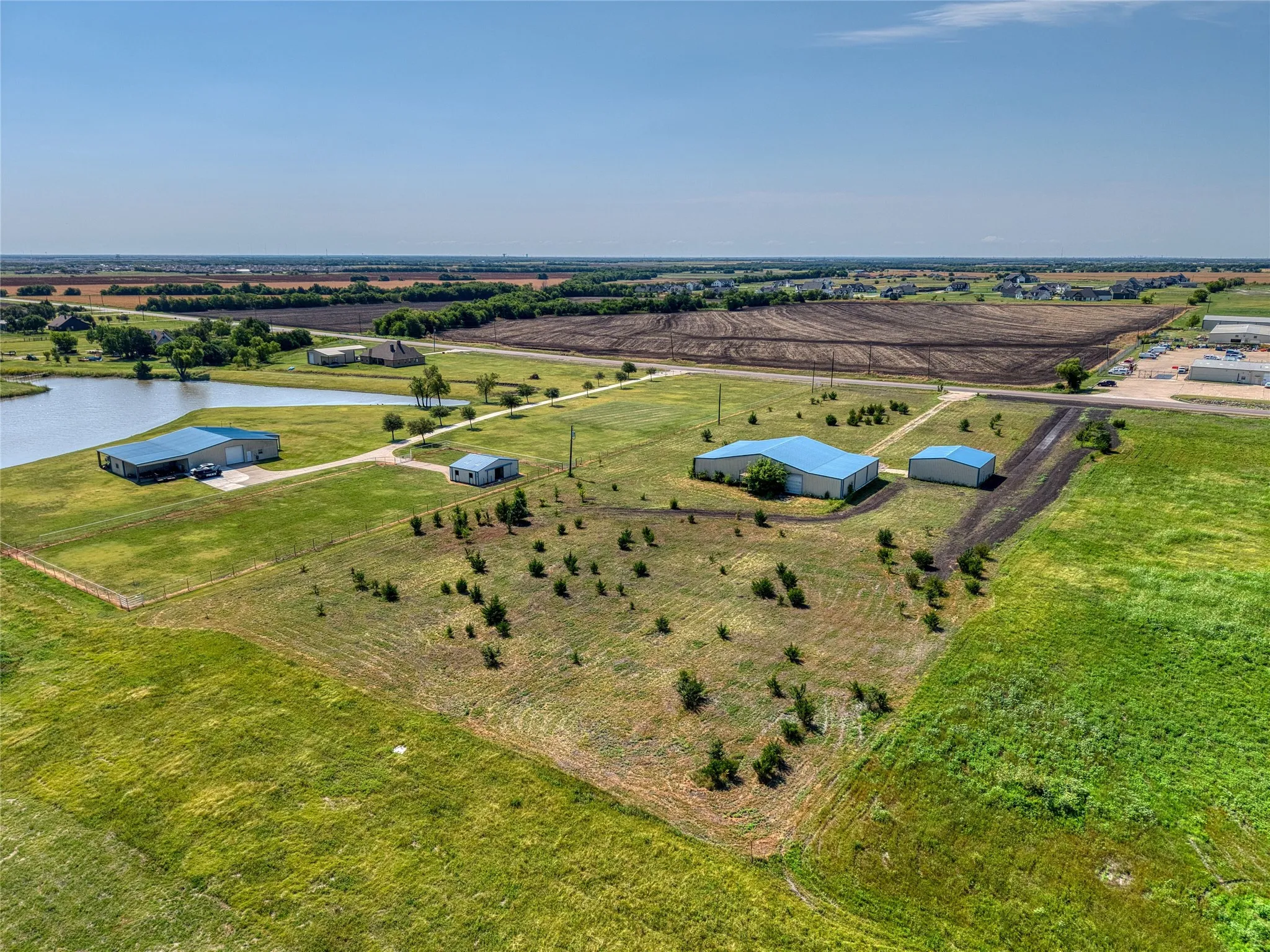 Expansive property featuring a tranquil pond, multiple structures with blue metal roofing, and surrounding open land