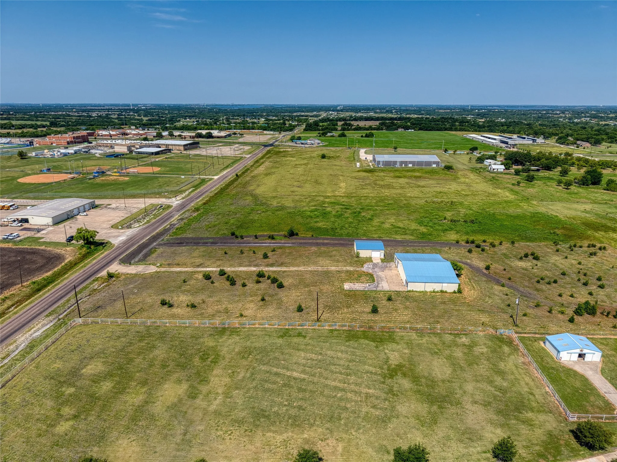 Expansive acreage featuring multiple outbuildings with blue metal roofs, a lengthy paved driveway, and open fields