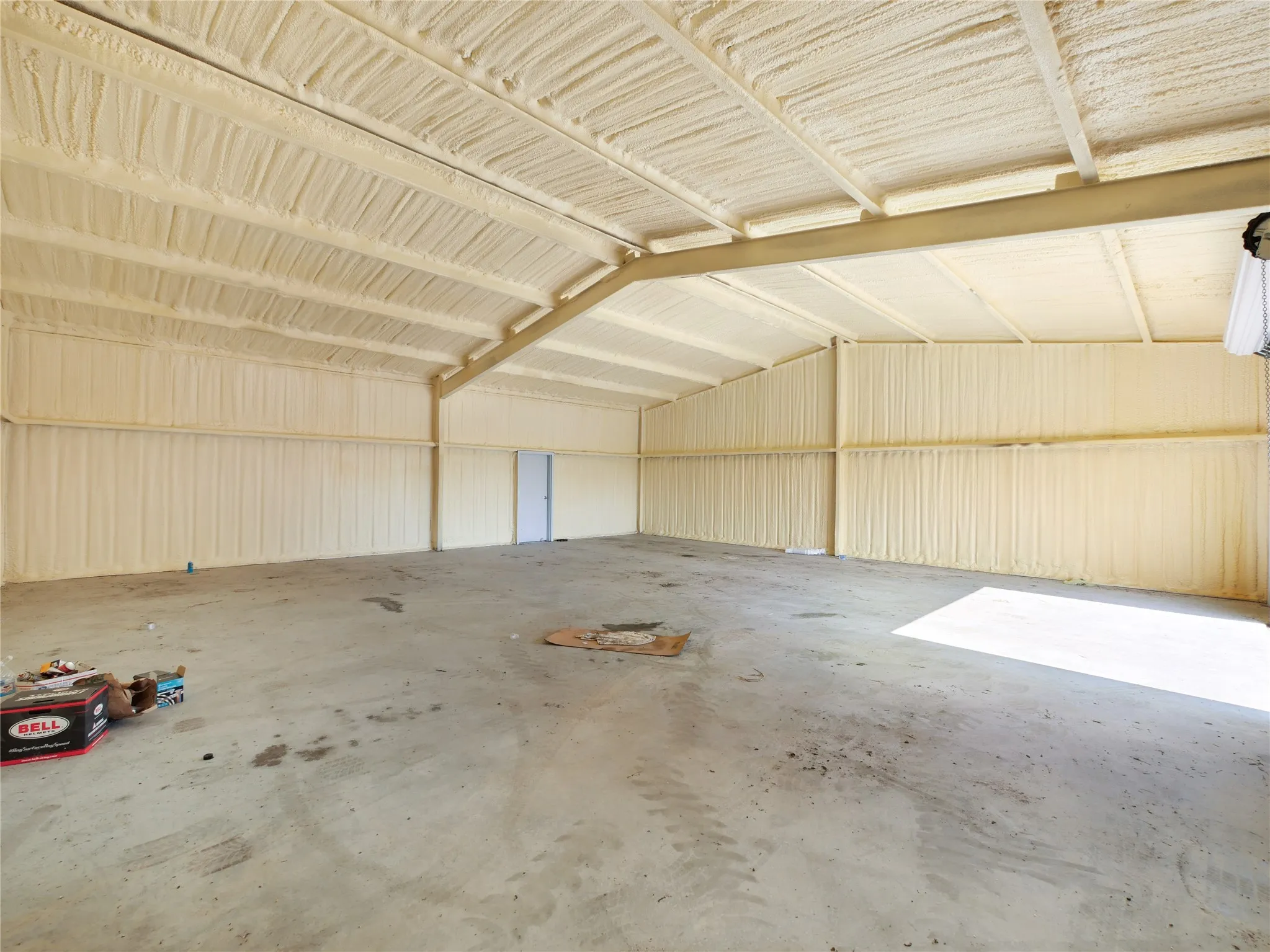 Open warehouse space with concrete flooring, exposed metal beam construction, and spray foam insulation on walls and ceiling