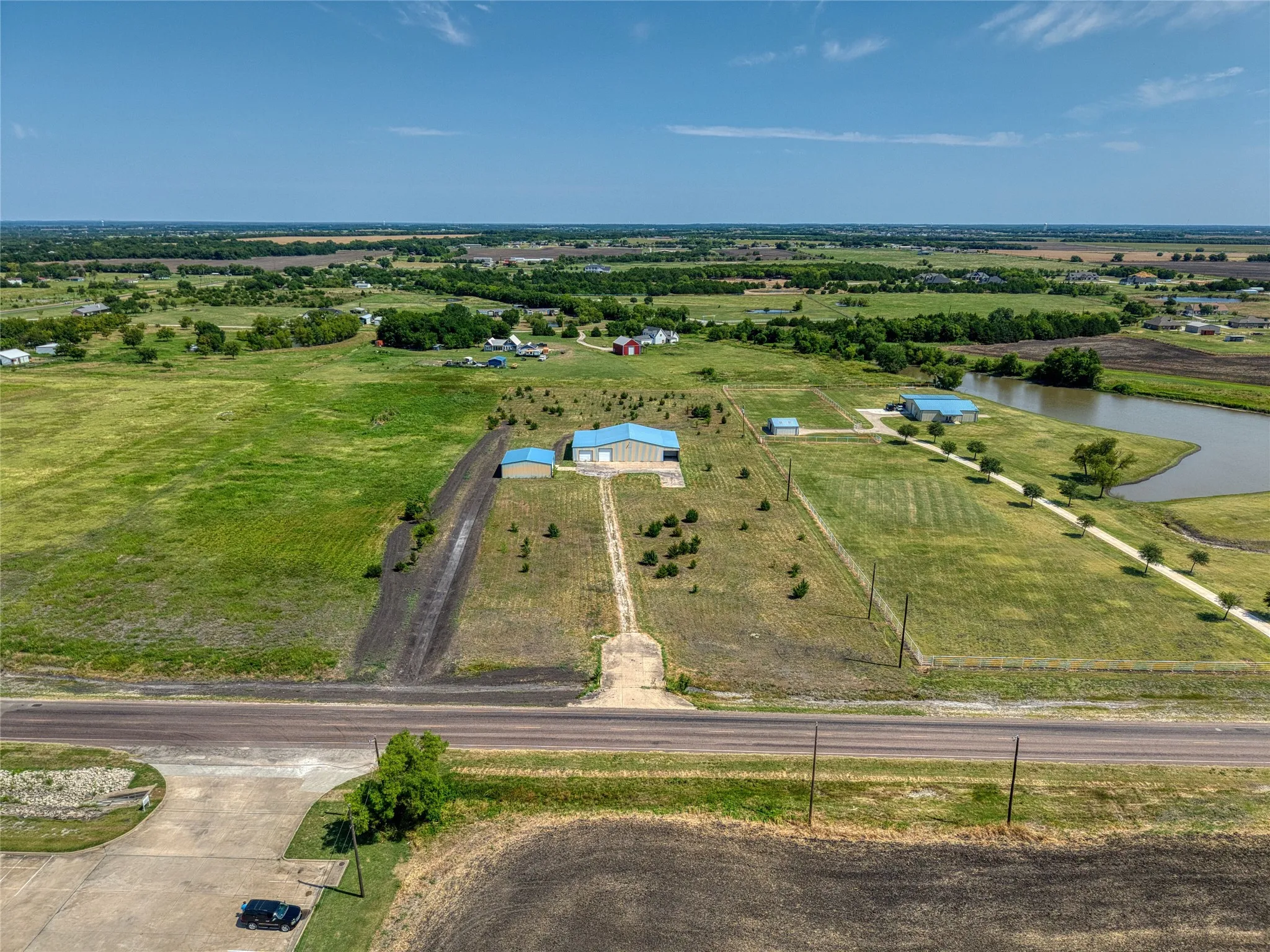 Expansive property featuring multiple outbuildings with light blue metal roofs, a private pond, and a long drive leading to the main structures