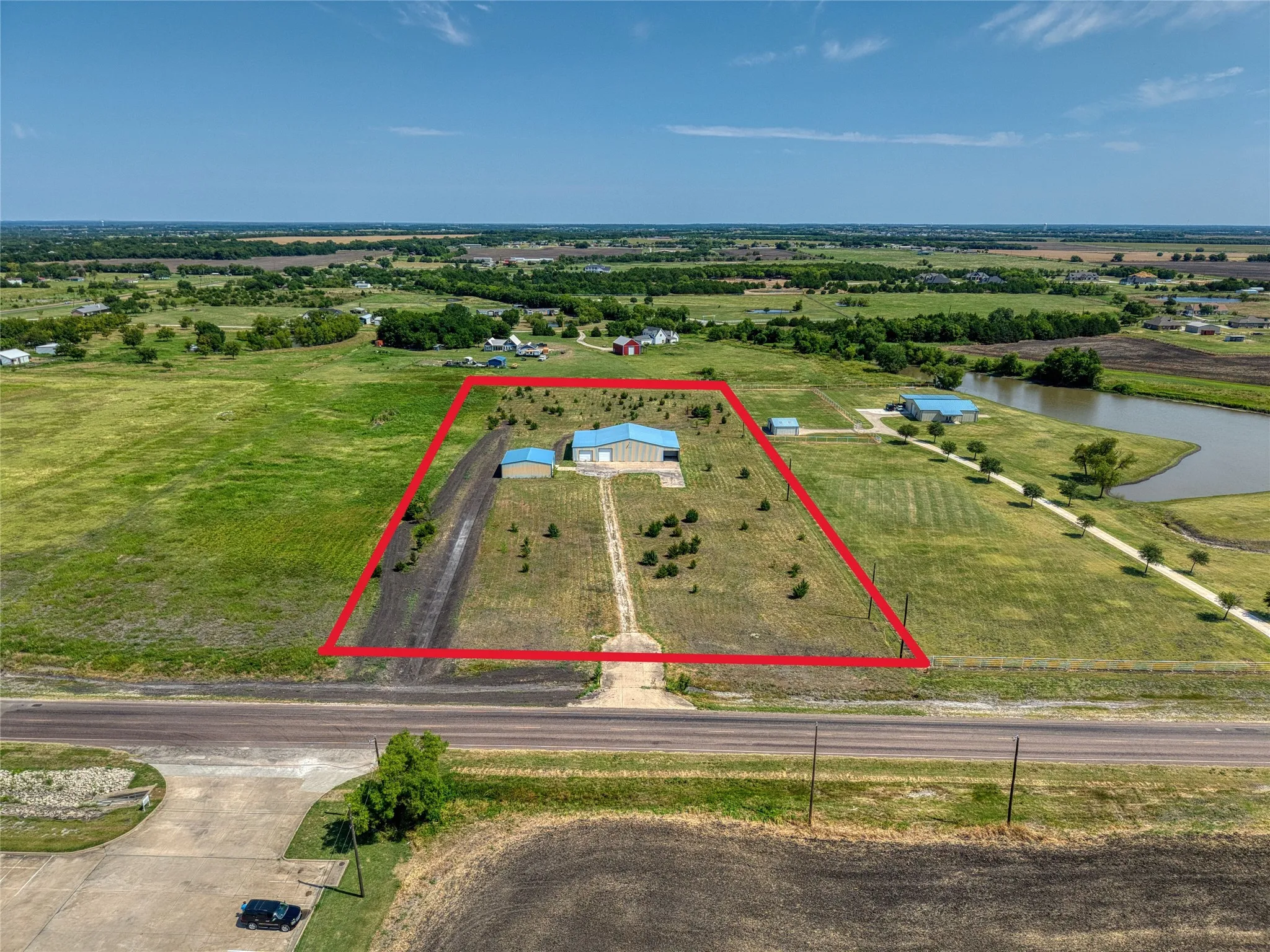 Expansive rural acreage featuring a main building with a light blue roof, an additional outbuilding, and a clear access road from the highway