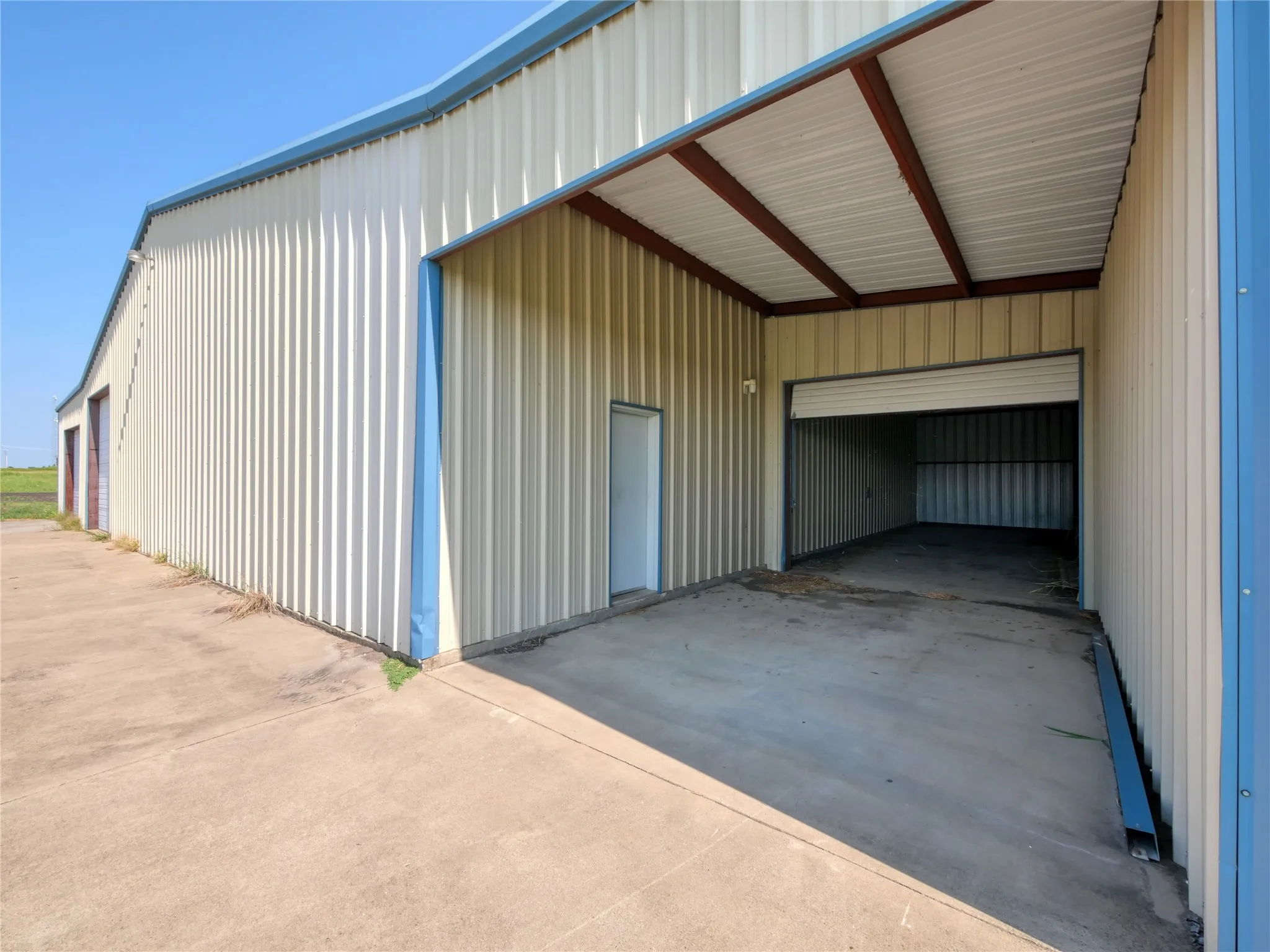 Corrugated metal siding with blue trim, concrete drive, and an overhead roll-up door