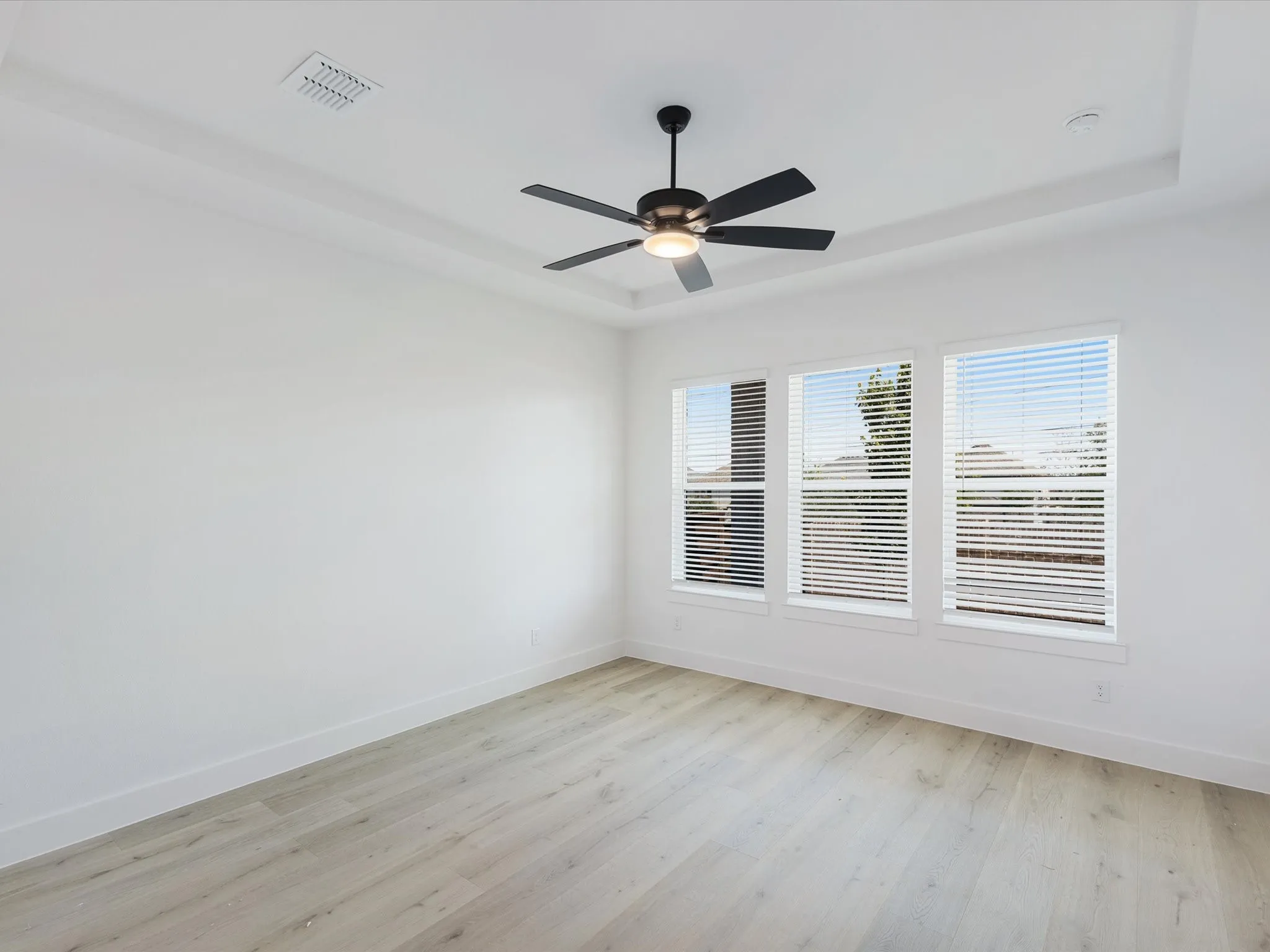 Primary Bedroom with light wood finished floors, a raised ceiling, and ceiling fan